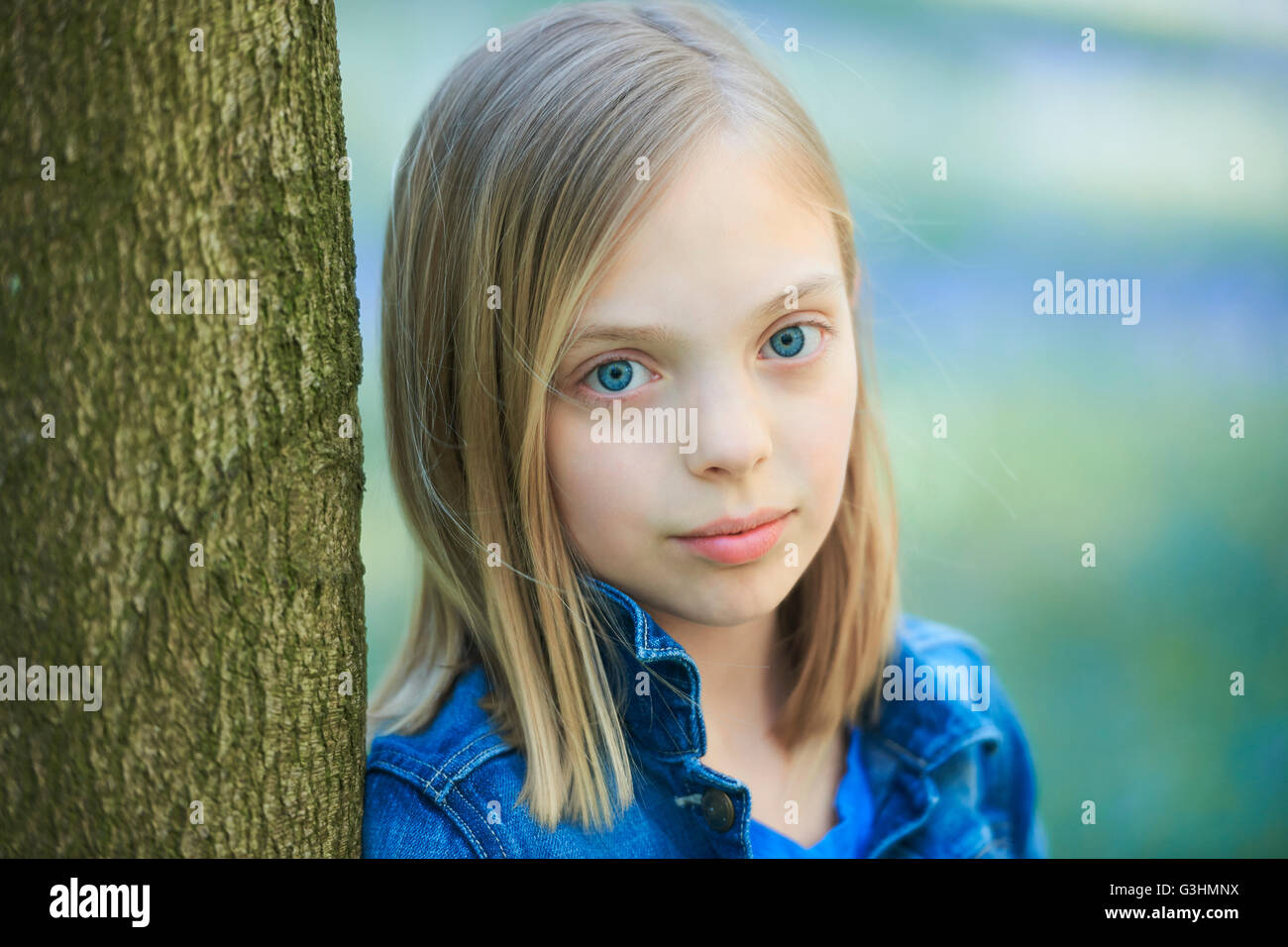 Portrait of blond haired girl leaning against tree in bluebell forest, Hallerbos, Brussels, Belgium Stock Photo