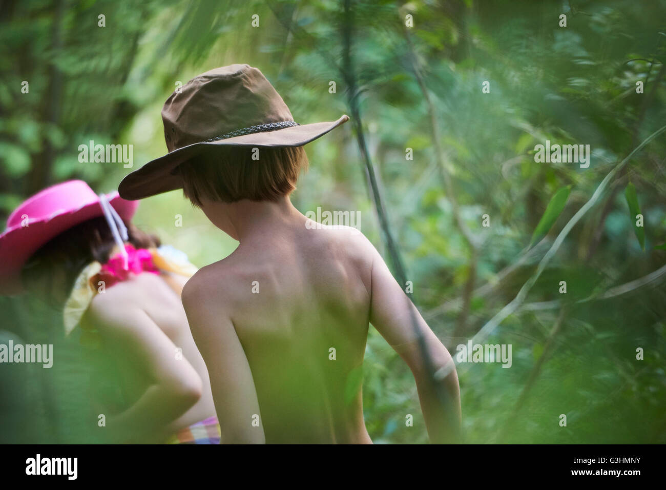 Rear view of girl and boy wearing cowboy hats playing in garden bushes Stock Photo