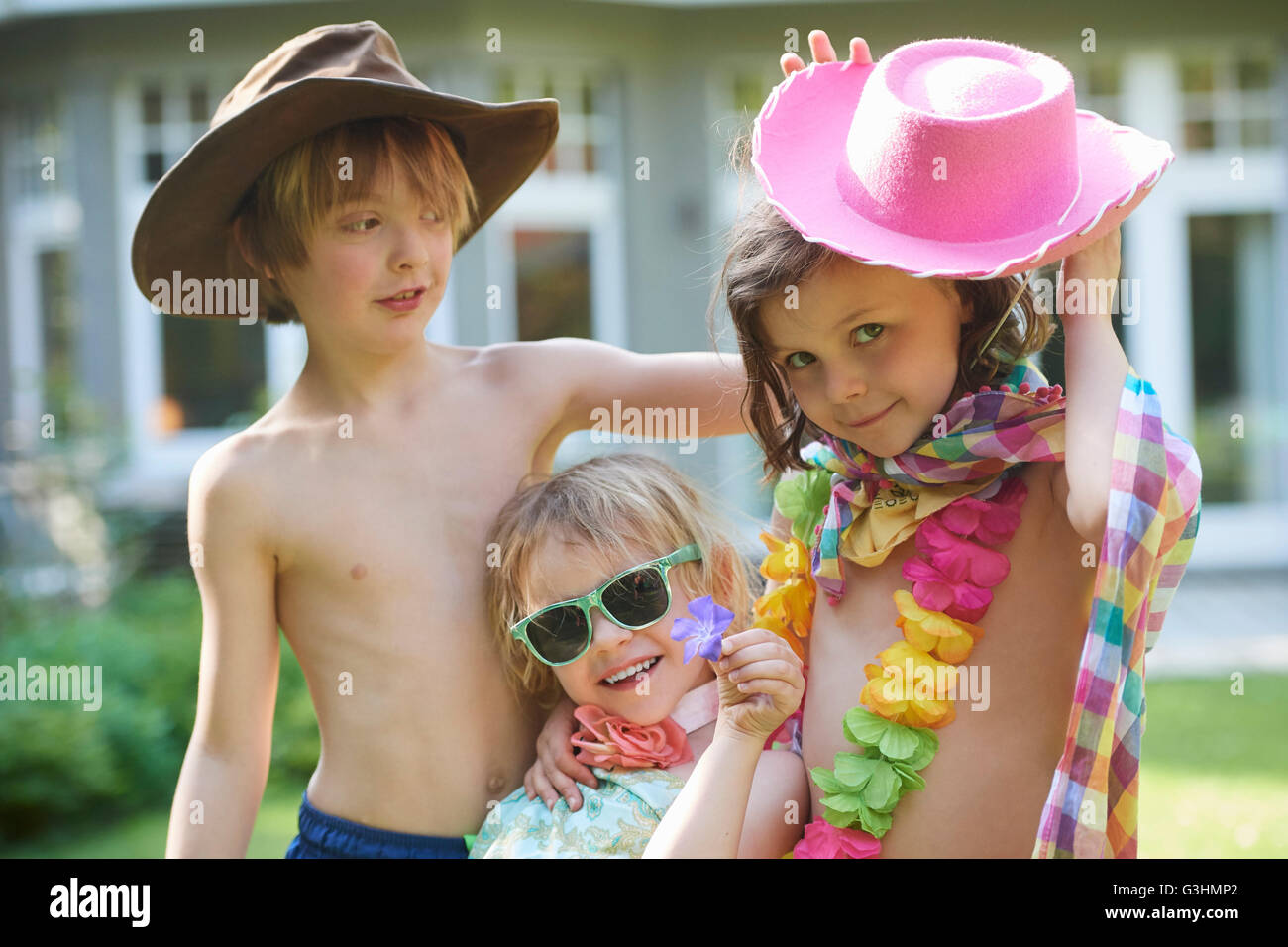 Portrait of girls and boy wearing cowboy hats and sunglasses in garden Stock Photo