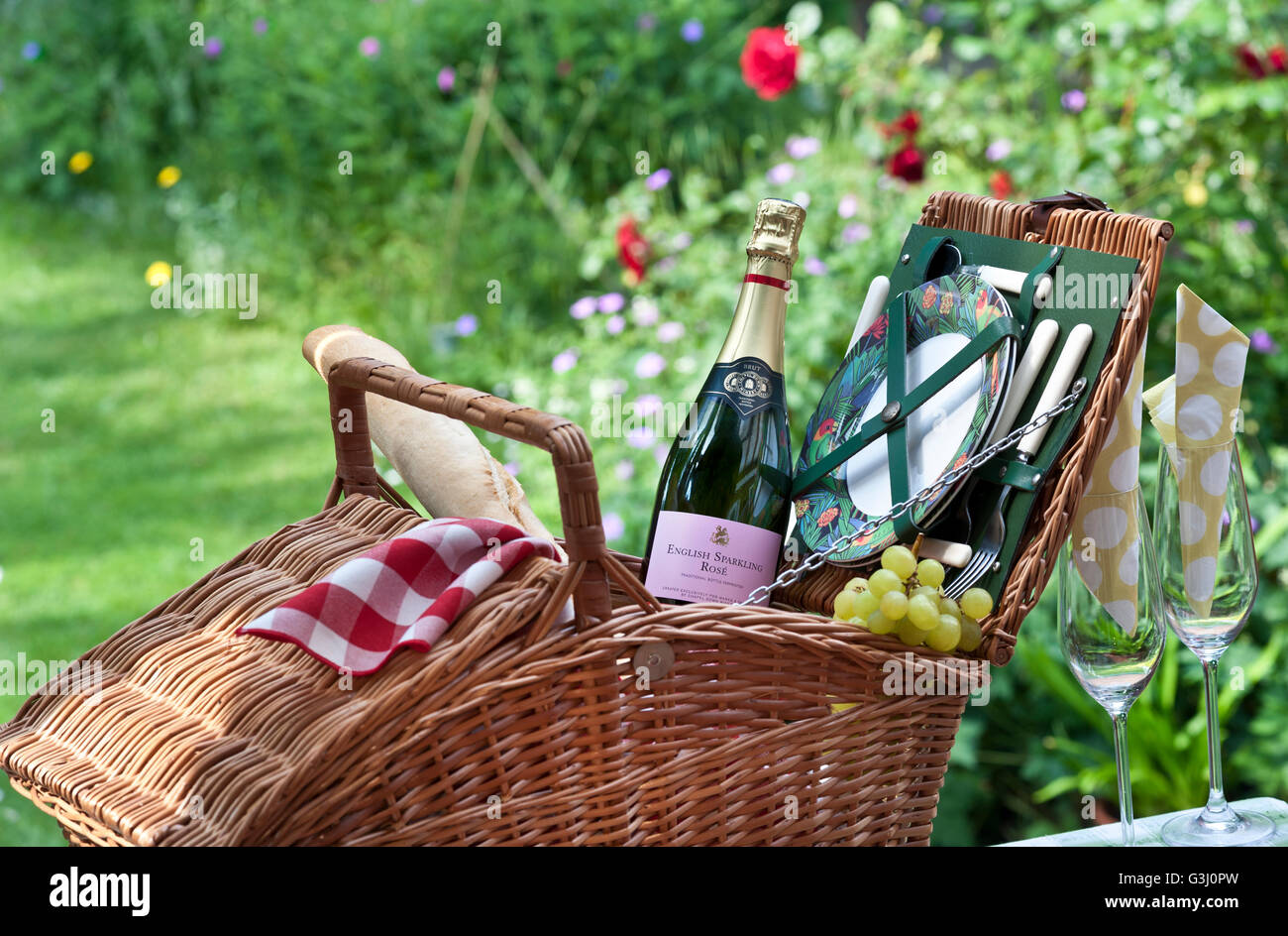 English sparkling Rose wine bottle and wicker picnic basket in sunny floral garden situation Stock Photo