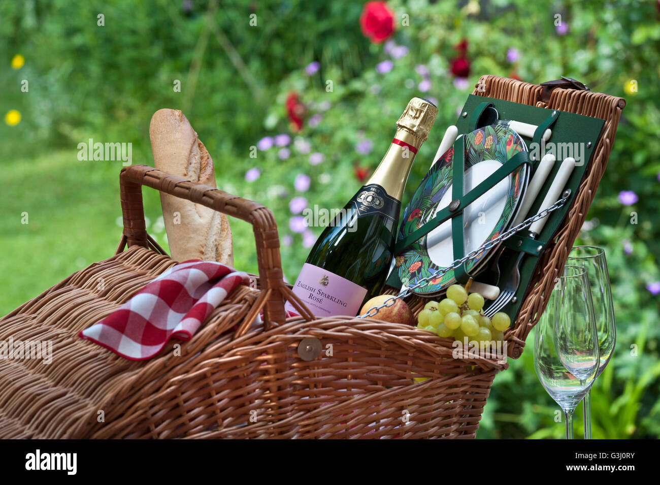 PICNIC HAMPER English sparkling Rosé wine bottle and wicker picnic basket in sunny floral garden situation Stock Photo