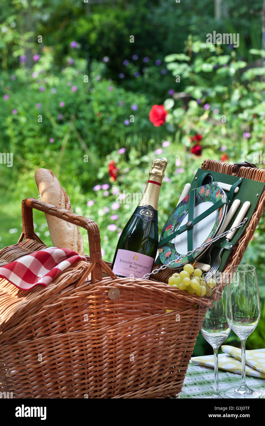 English sparkling Rosé Wine bottle and wicker picnic basket in sunny floral garden situation Stock Photo