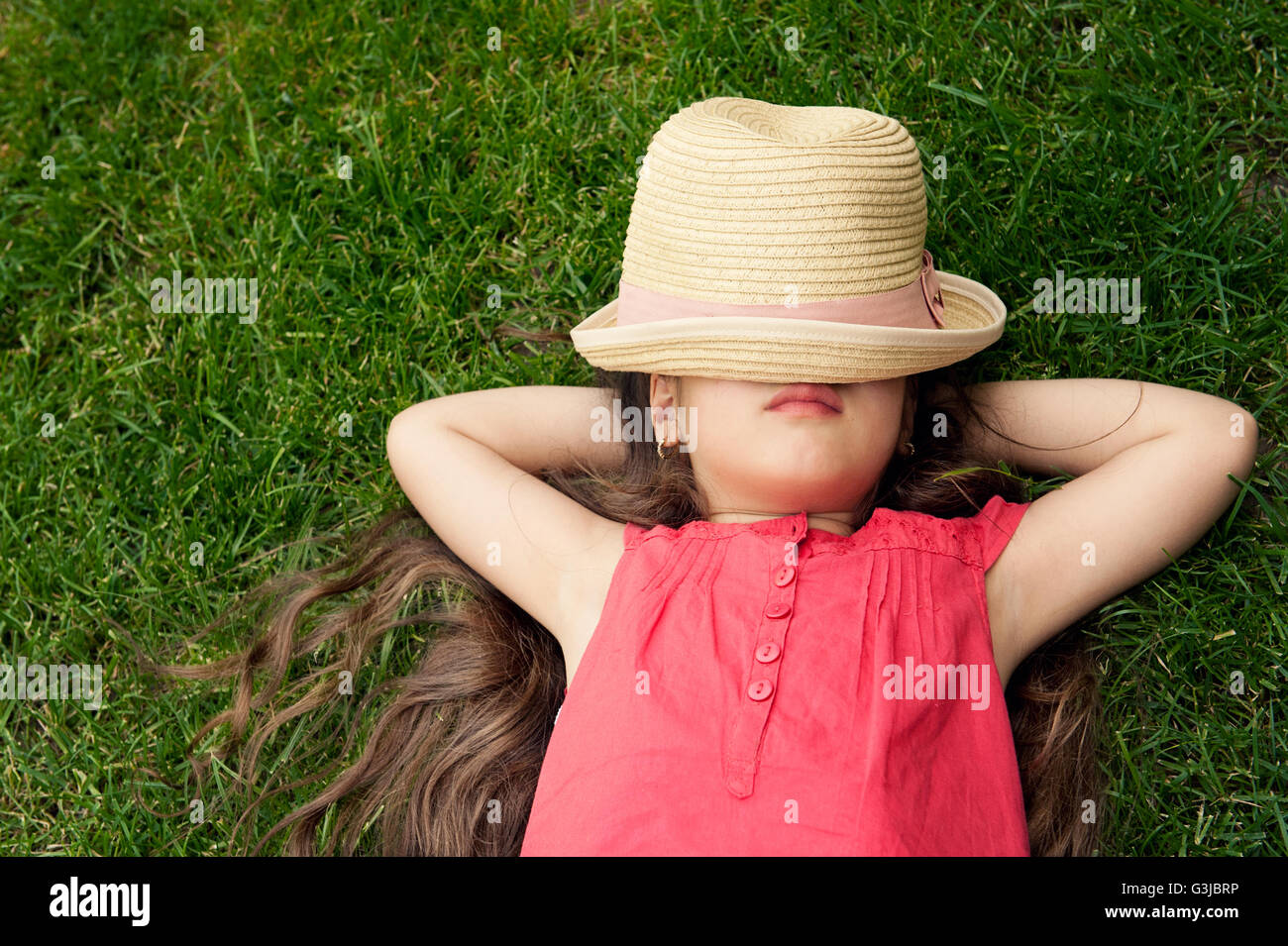 Child laying on grass,hat covering her face Stock Photo Alamy