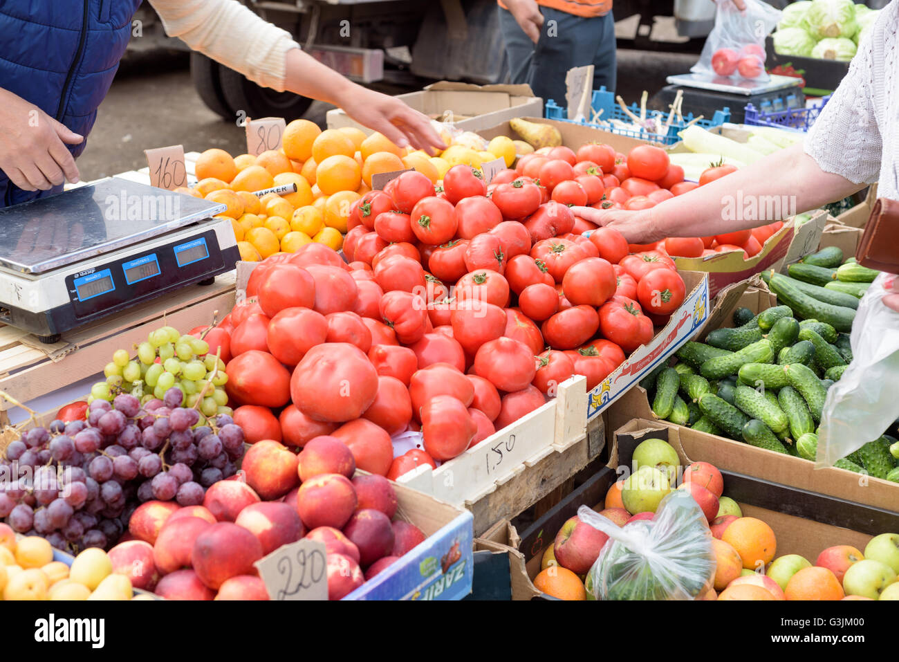 Local vegetable market stall selling fresh produce with peoples arms choosing and selecting ripe tomatoes from a selection of pr Stock Photo