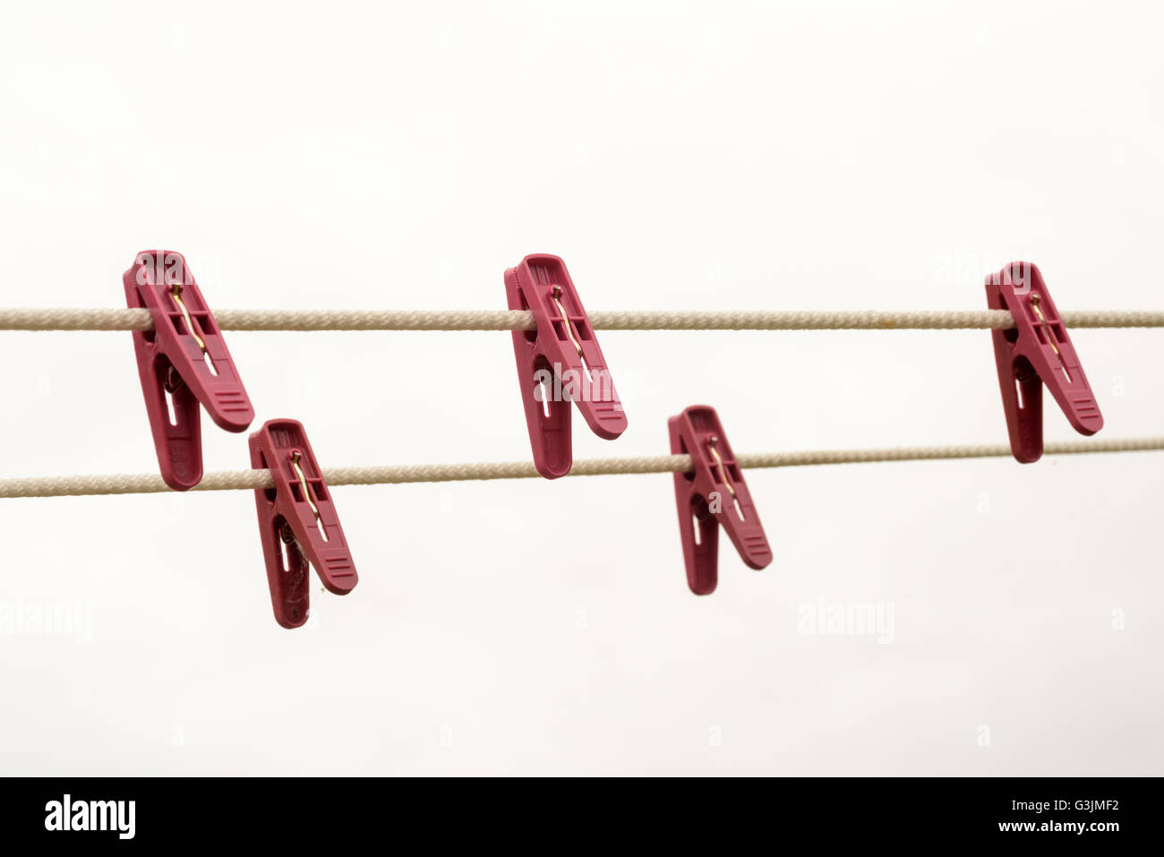 Five red plastic pegs hanging on a washing-line with a white overcast sky background. domestic home based choir background with Stock Photo