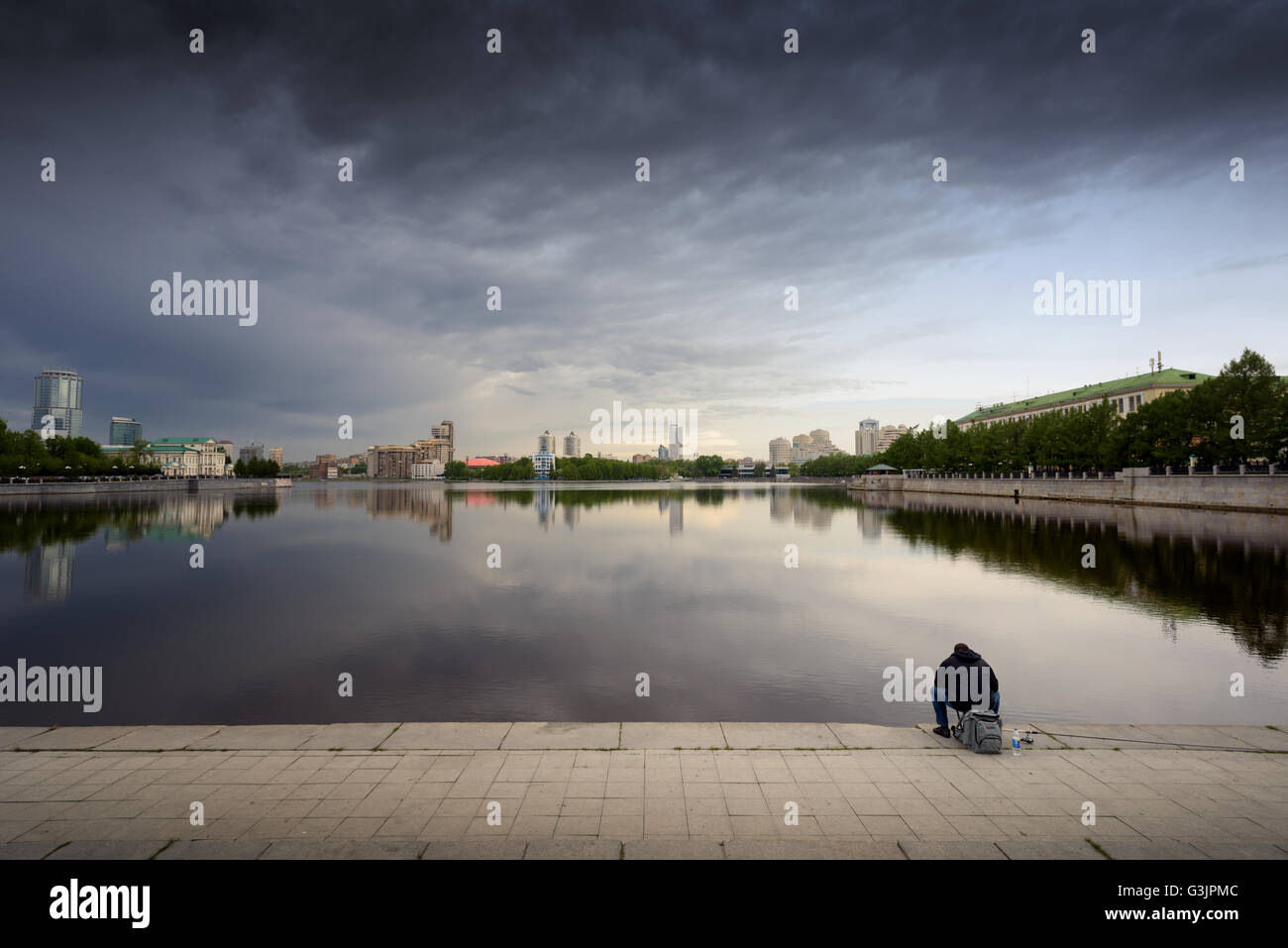 Single man sits and fishes in the City Pond in Yekaterinburg. The vast stretch of water is a key tourist attraction for people Stock Photo