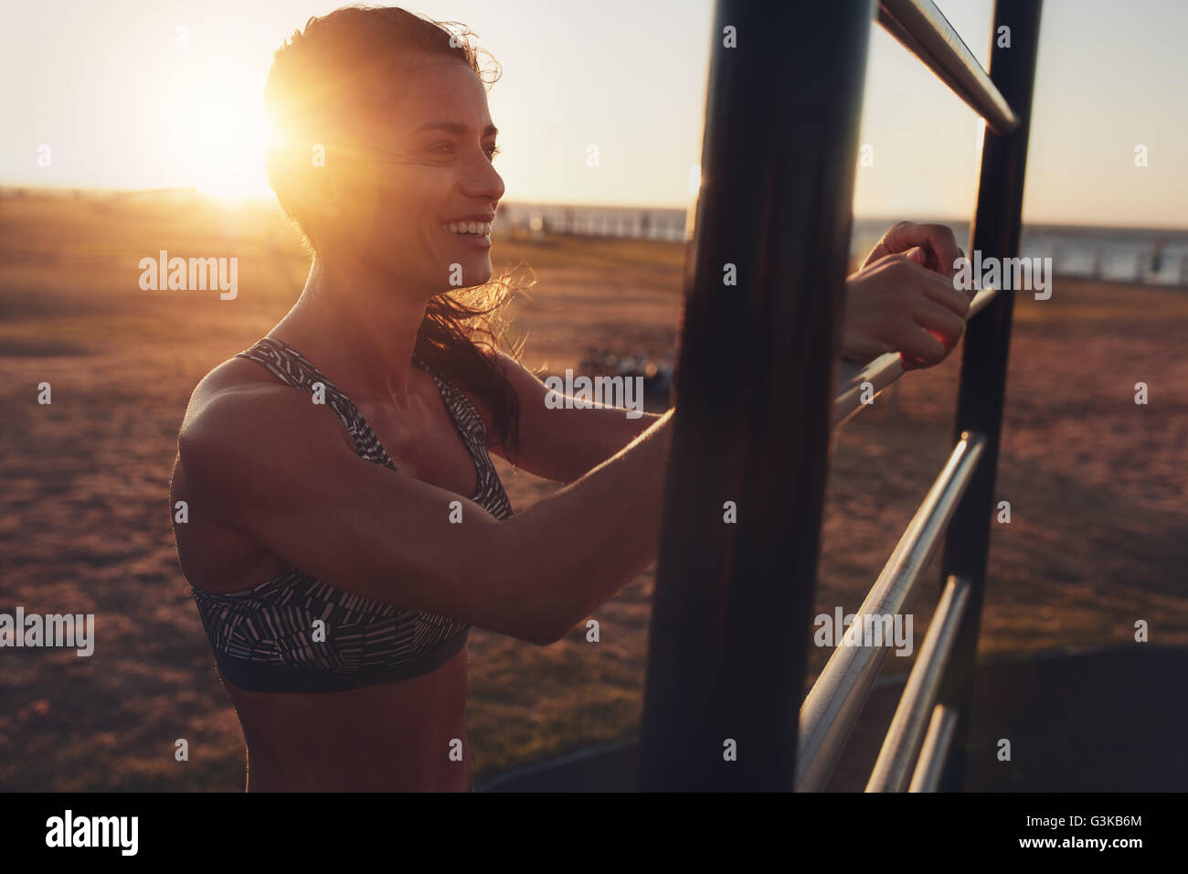 Happy young sportswoman working out on wall bars during sunset. fitness woman smiling and looking away at evening. Stock Photo