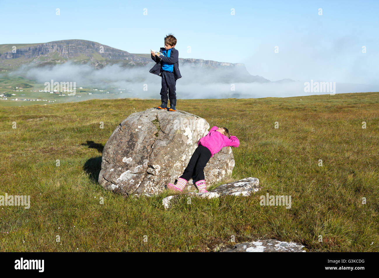 Girl relaxing on a rock and boy reading a map during a countryside walk on the Isle of Skye, Inner Hebrides, Scotland, UK Stock Photo