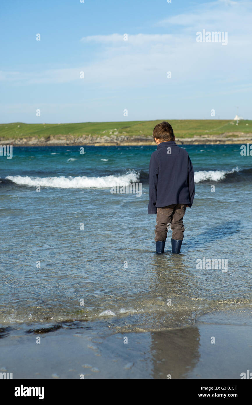 Boy wearing boots standing in water on isolated beach, Isle of Lewis, Outer Hebrides, Scotland, UK, Europe Stock Photo