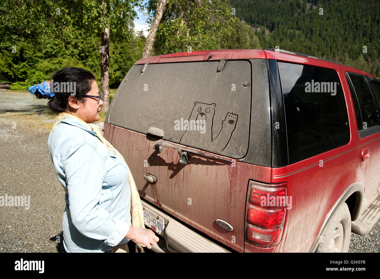 A woman draws a bear in dirt on the back of a Truck, Birkenhead Provincial Park, north of Pemberton, British Columbia, Canada. Stock Photo