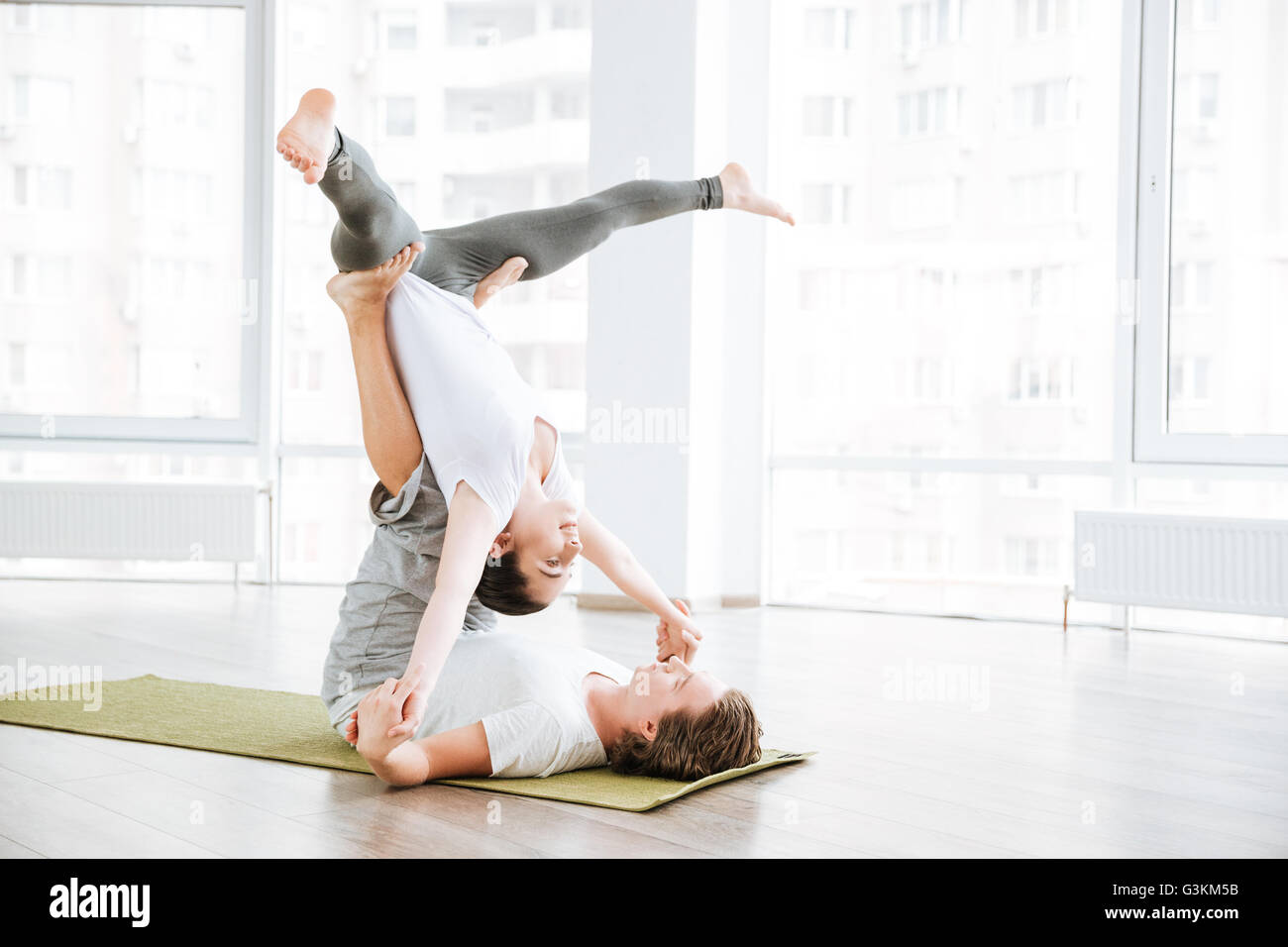 Beautiful young couple doing acrobatic yoga position in studio together ...