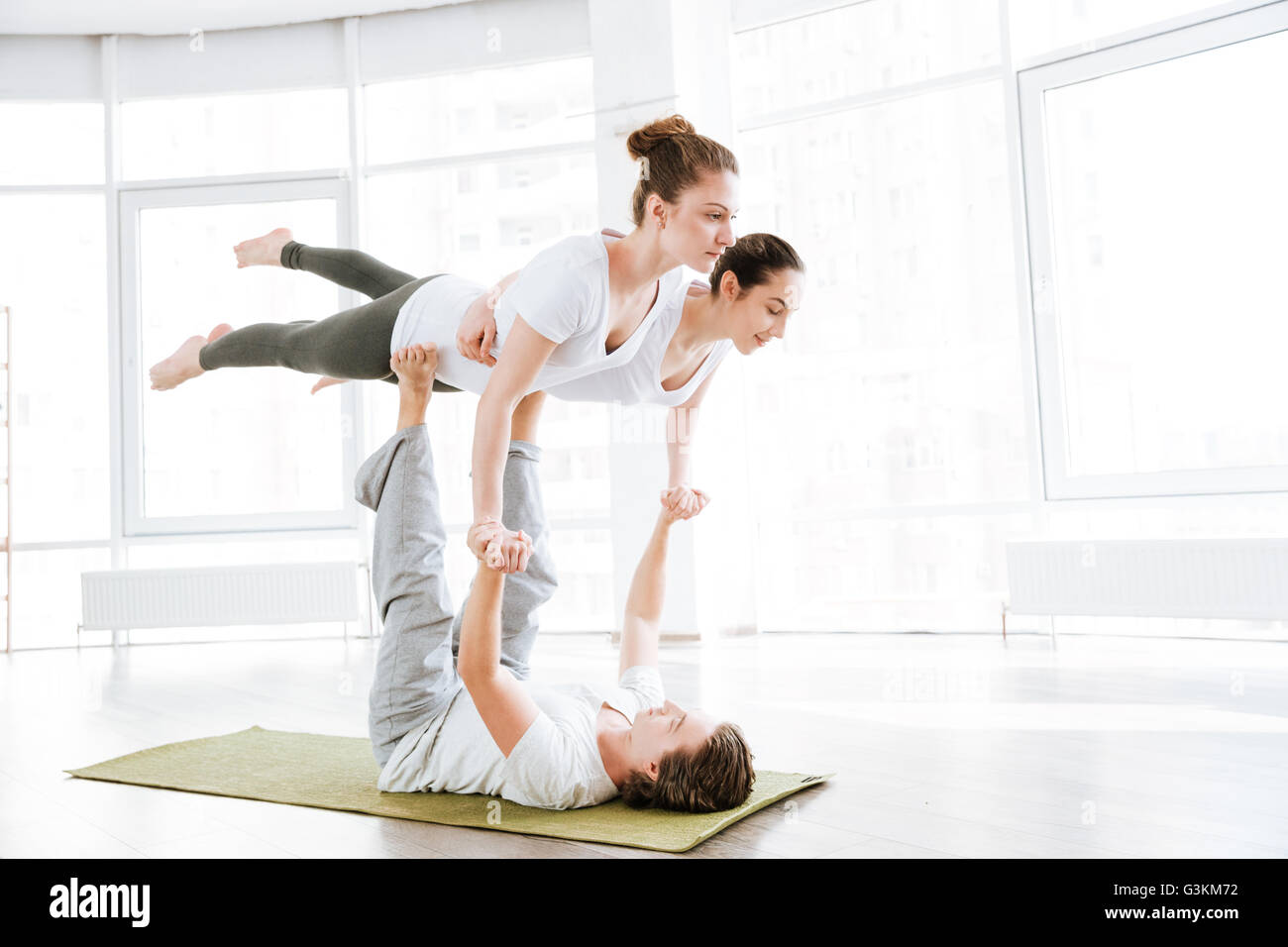 Group of two young women and man balancing and doing acro yoga in studio Stock Photo
