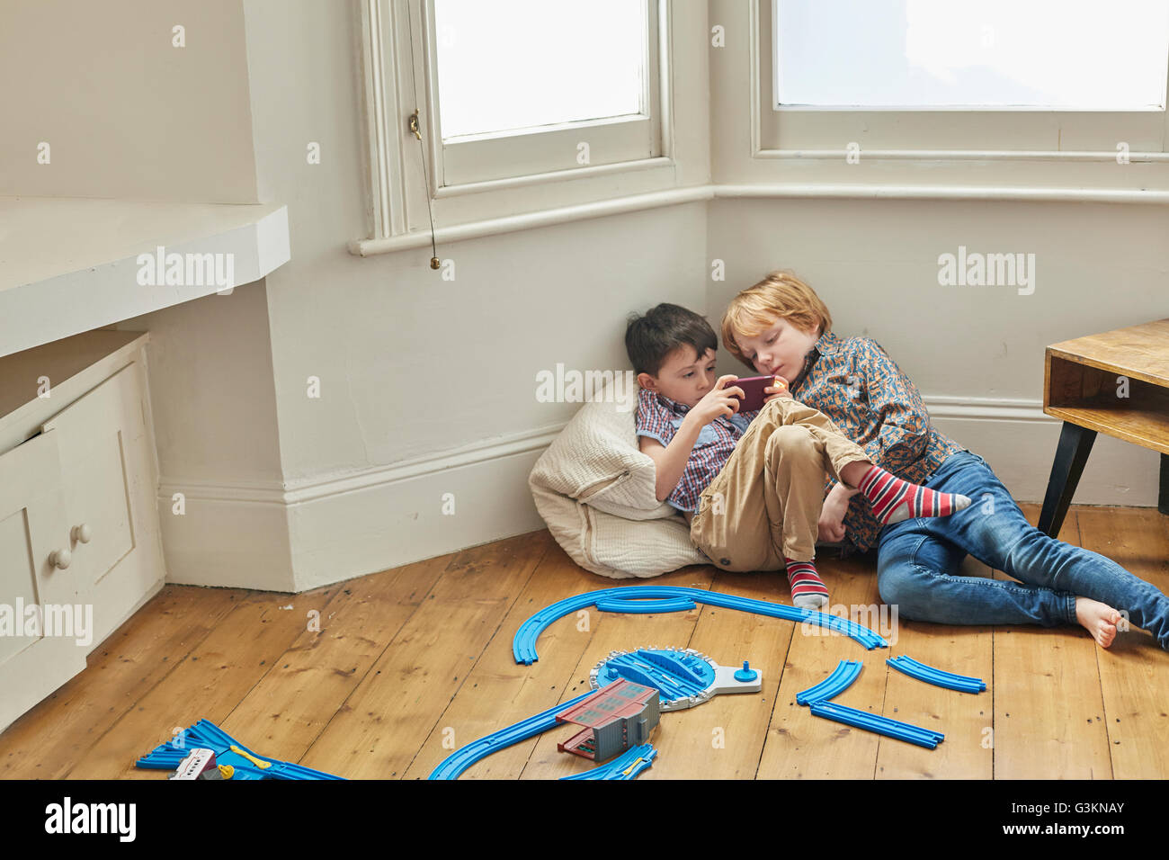 Two young boys, sitting indoors, looking at smartphone Stock Photo