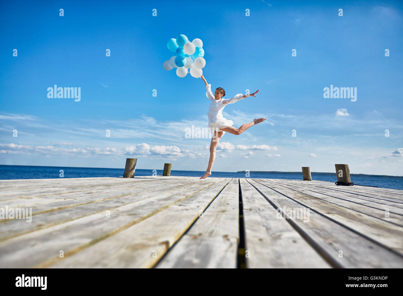 Young woman dancing on wooden pier, holding bunch of balloons Stock Photo