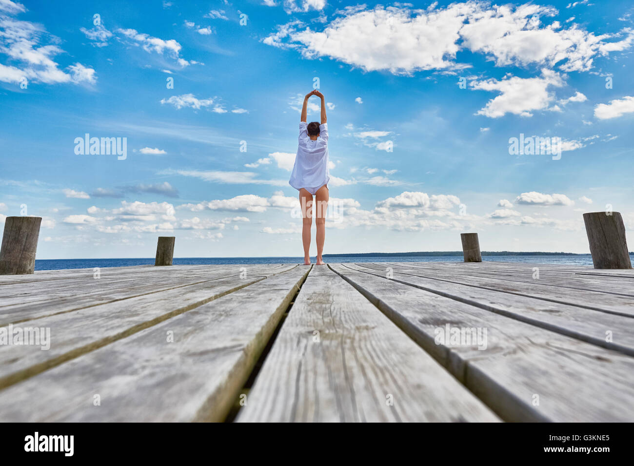 Young woman standing on wooden pier, stretching, rear view Stock Photo