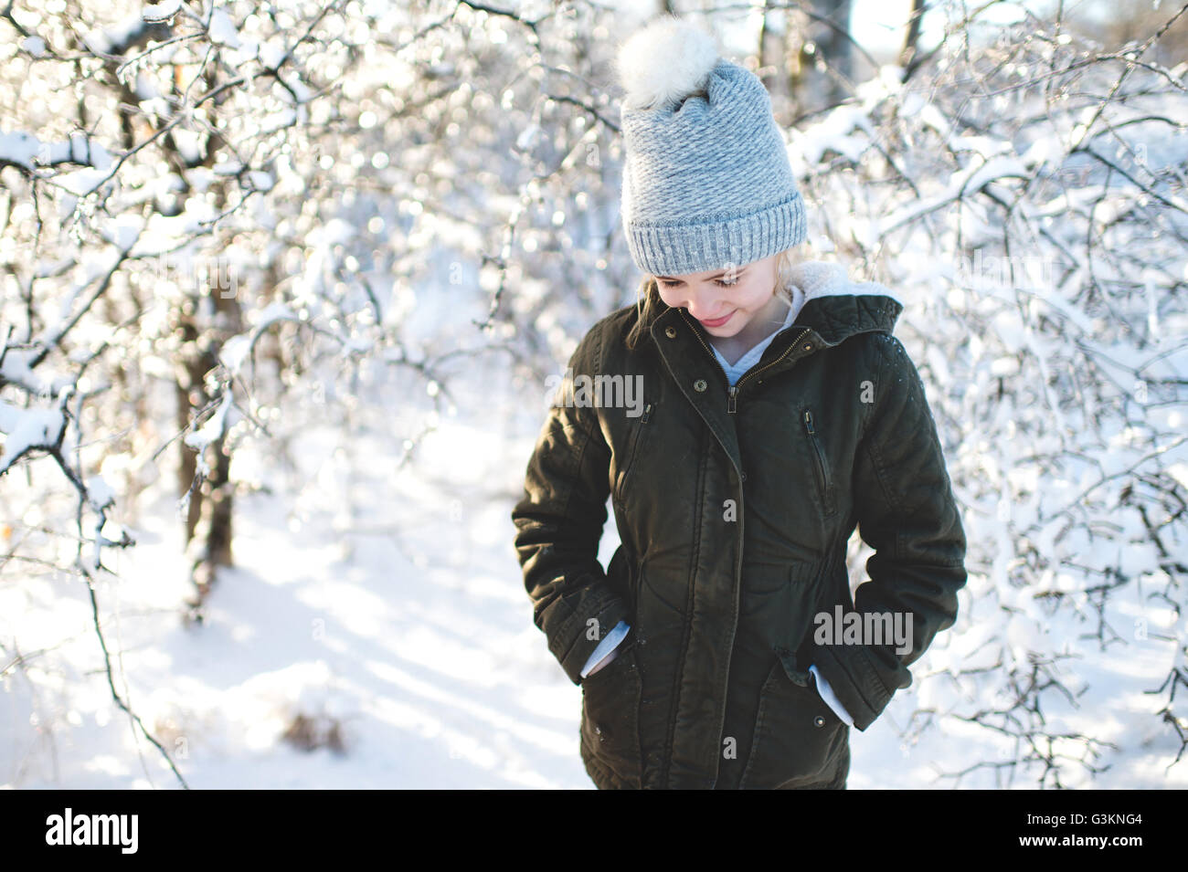 Young girl in snowy landscape, hands in pockets, looking down Stock Photo