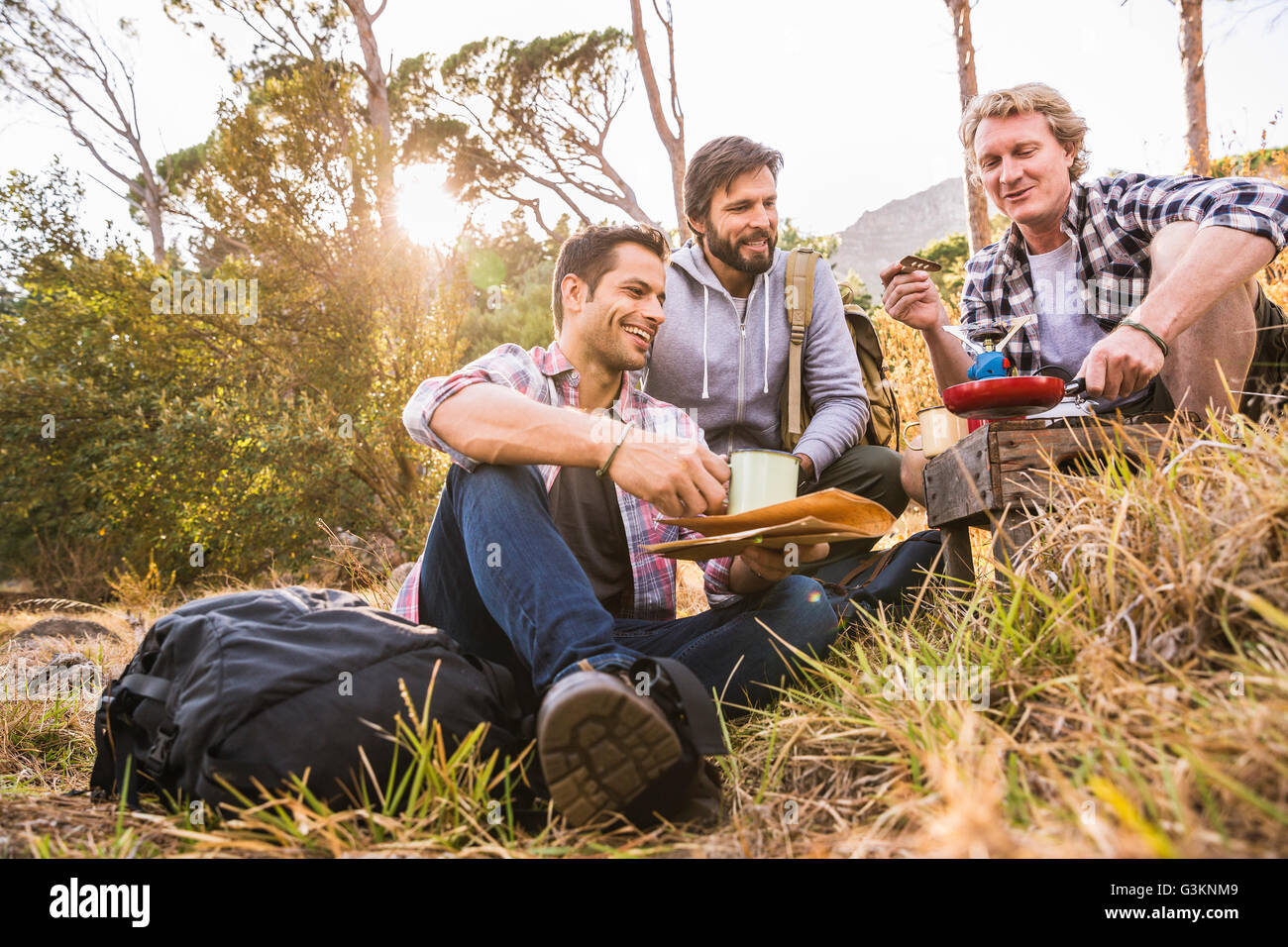 Three men frying breakfast on camping stove in forest, Deer Park, Cape Town, South Africa Stock Photo