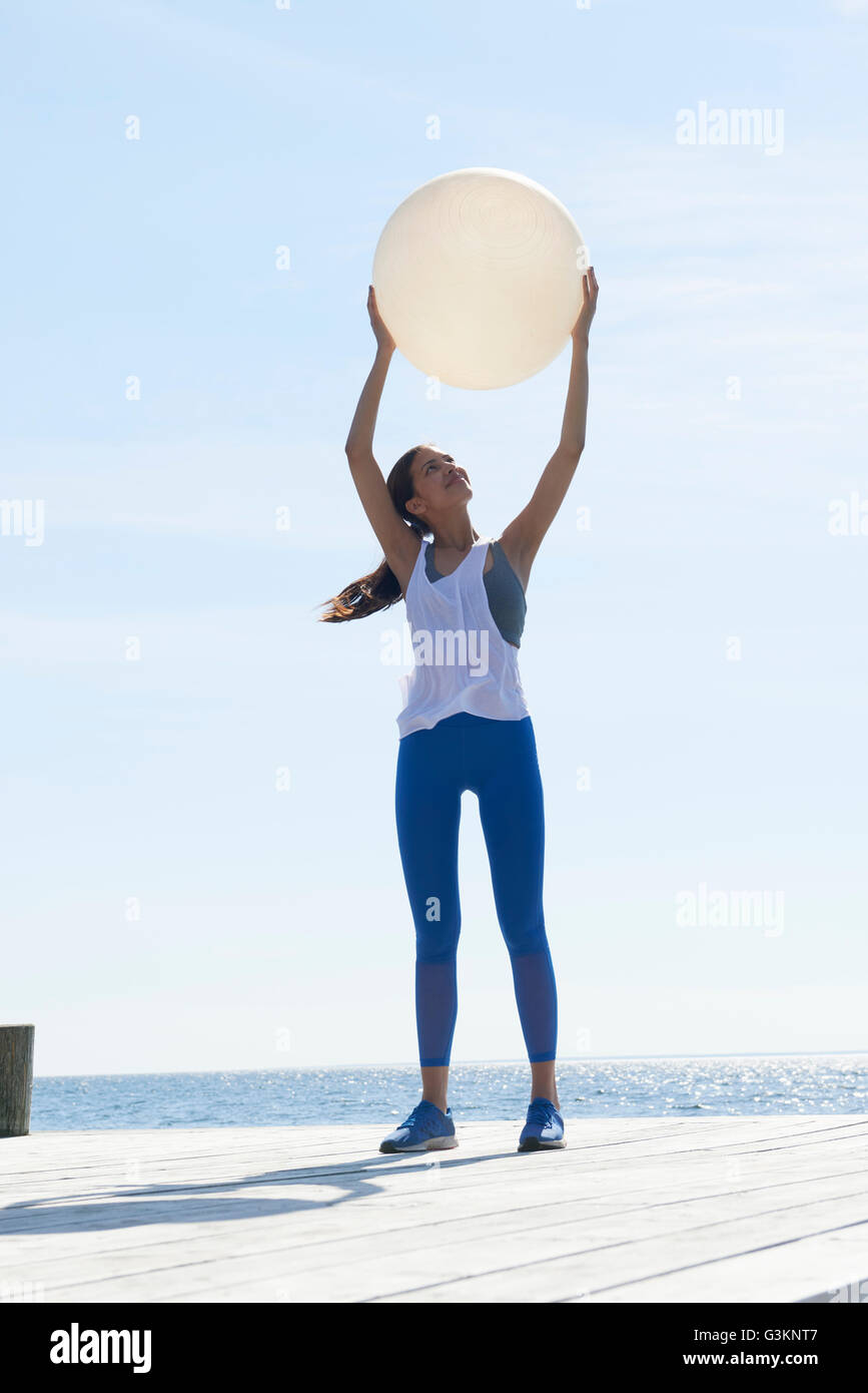 Women wearing sports clothes standing on pier arms raised holding exercise ball Stock Photo