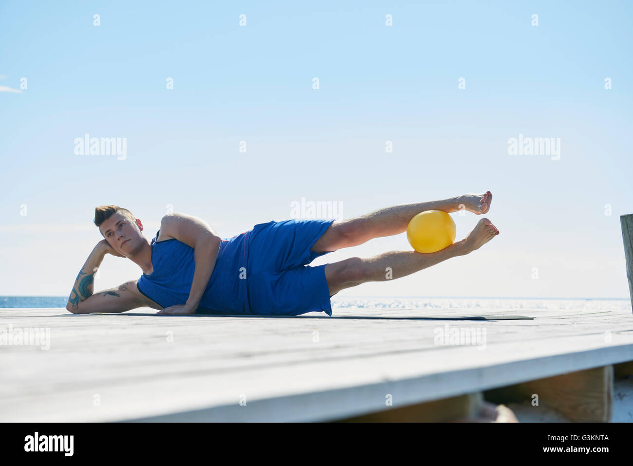 Man on pier lying on side resting on elbow, ball between legs Stock Photo