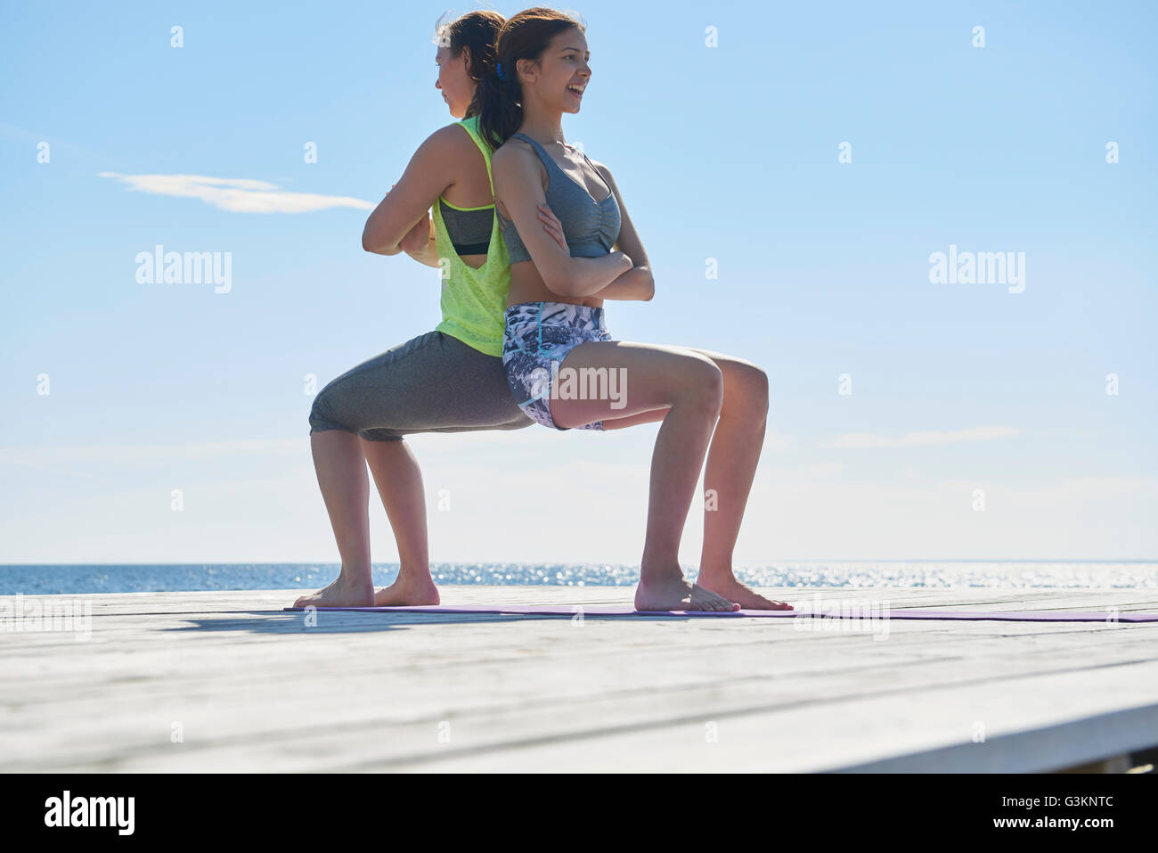 Women crouching on pier back to back arms crossed Stock Photo