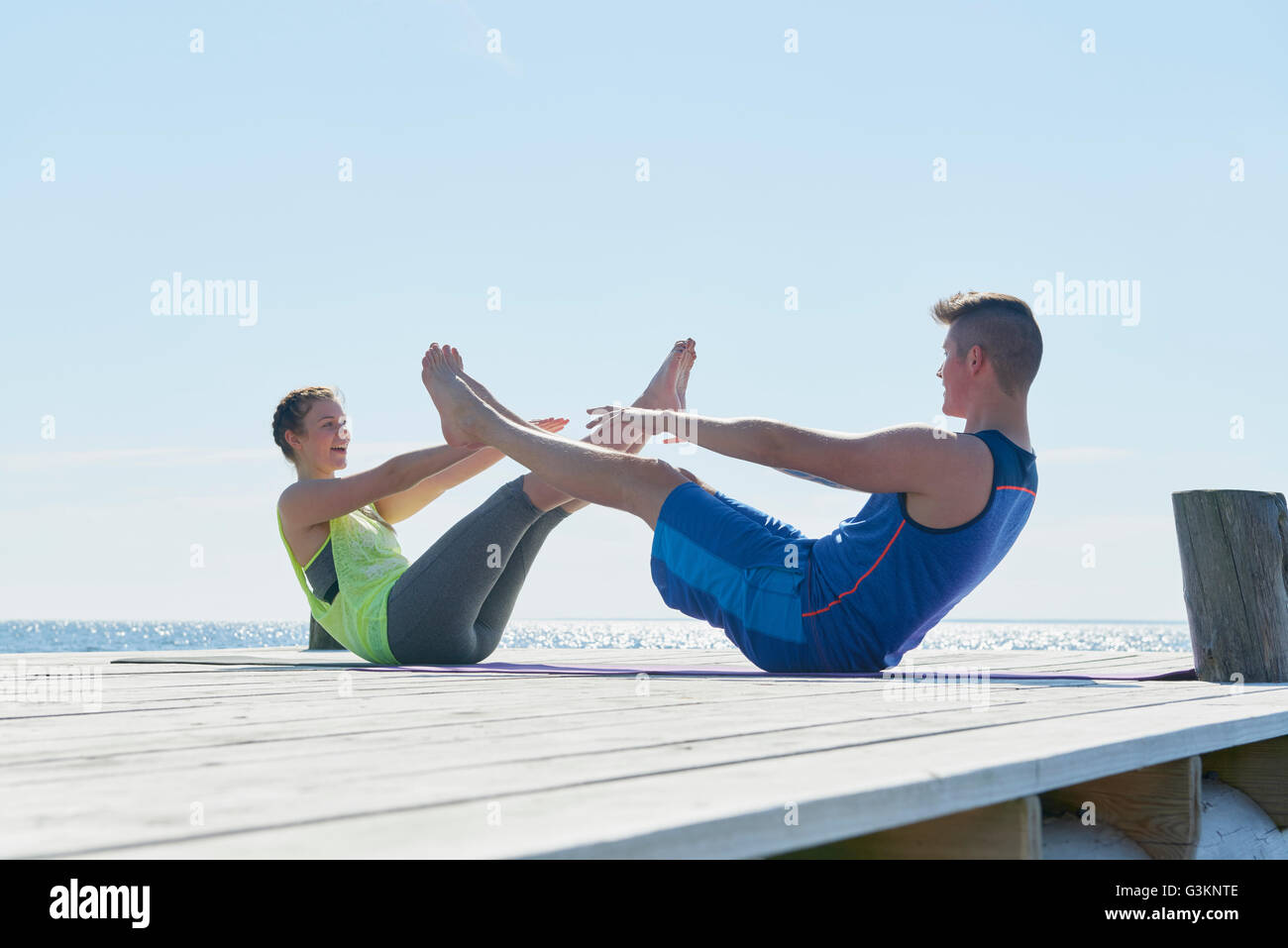 Couple on pier face to face, legs raised doing sit ups Stock Photo
