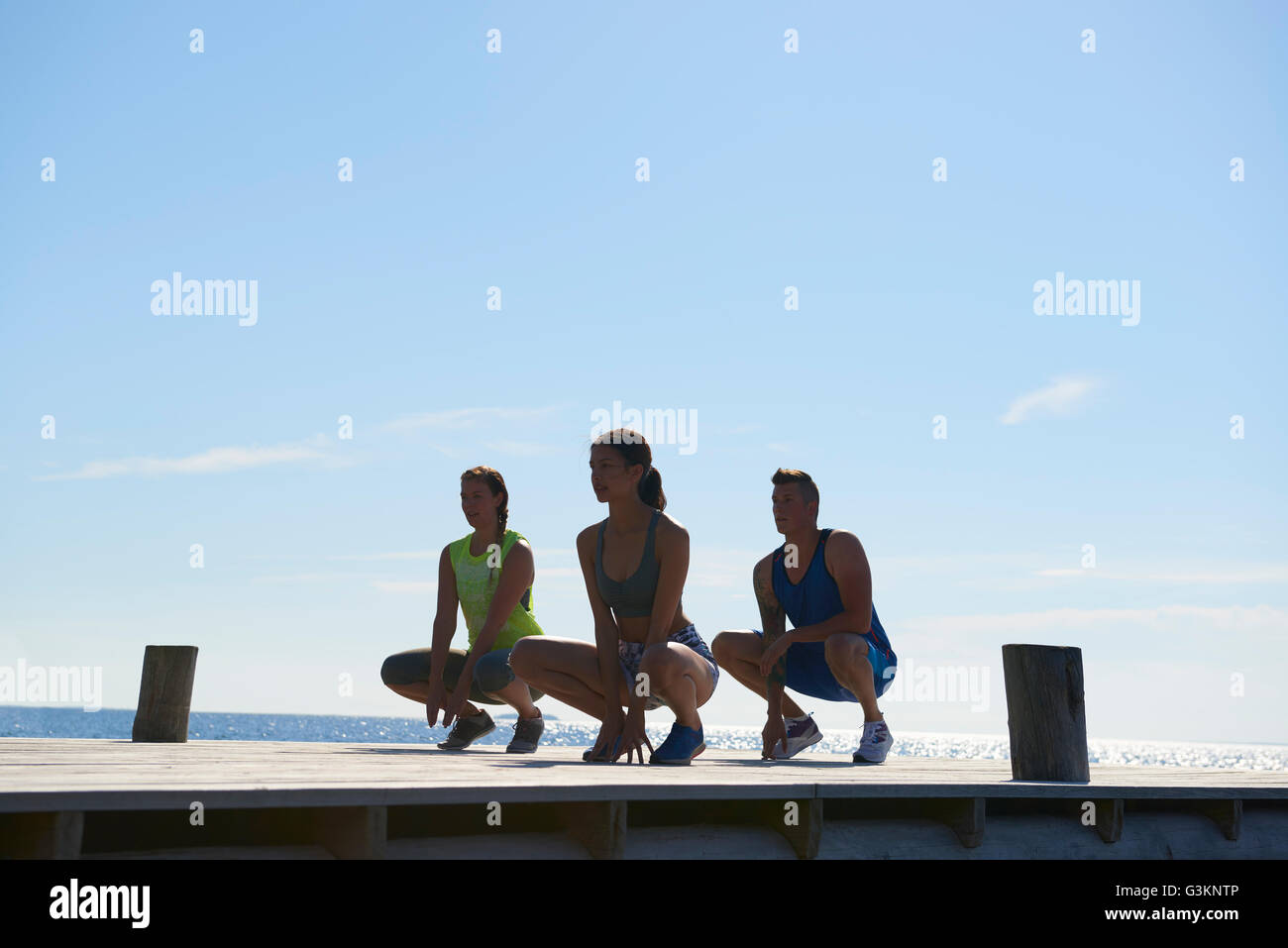Friends on pier wearing exercise clothes crouching looking away Stock Photo