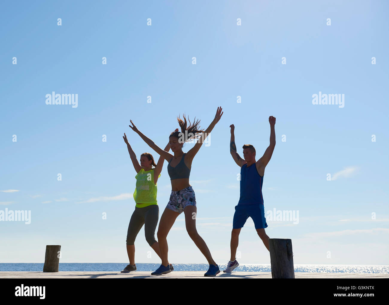 Friends on pier wearing exercise clothes arms raised exercising Stock Photo