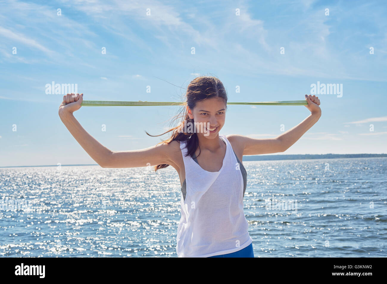 Woman in front of ocean holding resistance band looking at camera smiling Stock Photo