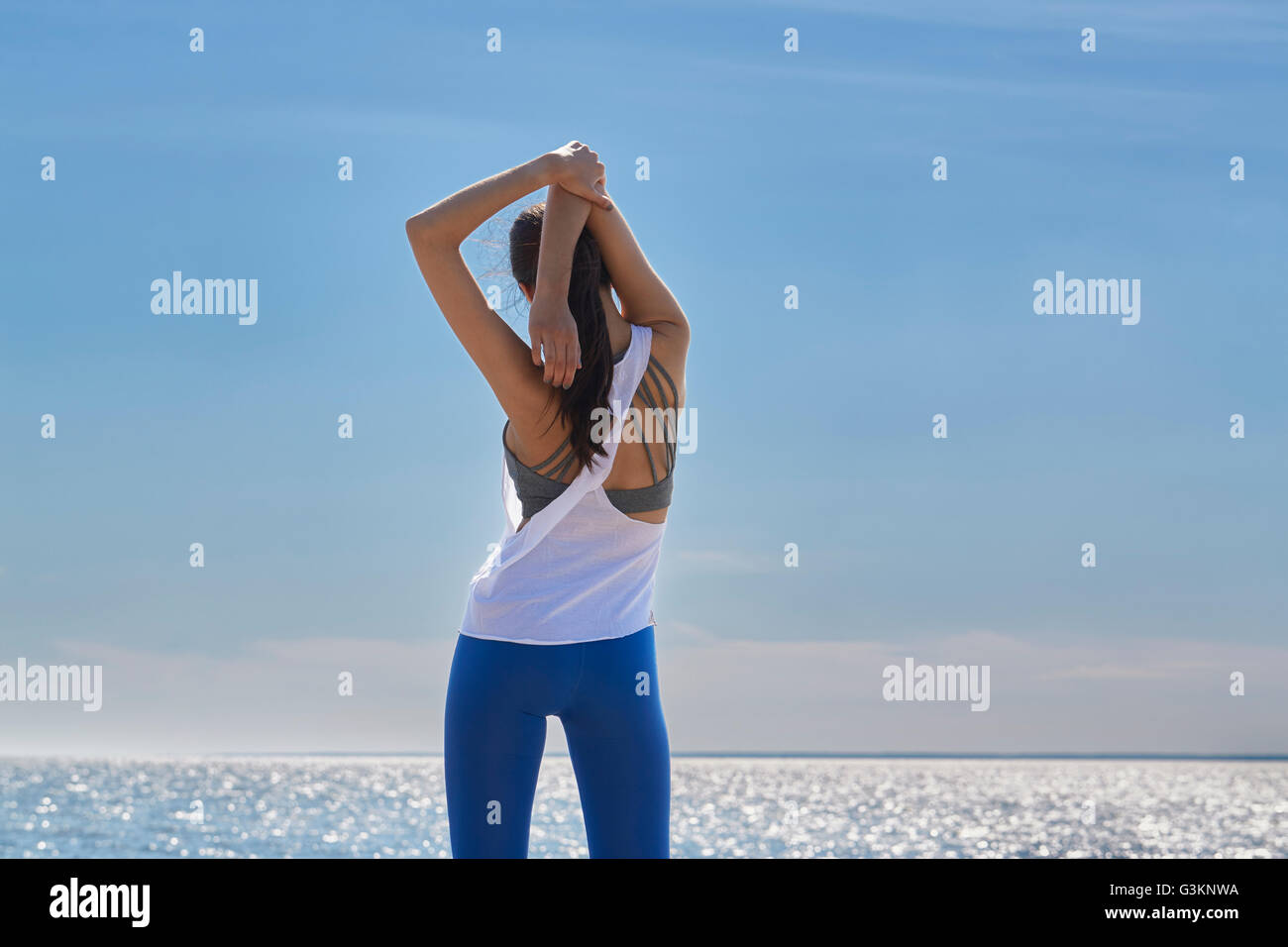 Rear view of young woman arms raised hands behind head stretching Stock Photo