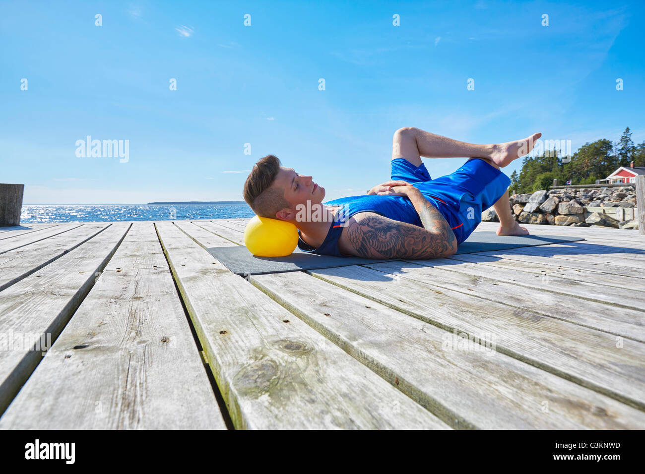Tattooed man lying on pier using ball as pillow Stock Photo