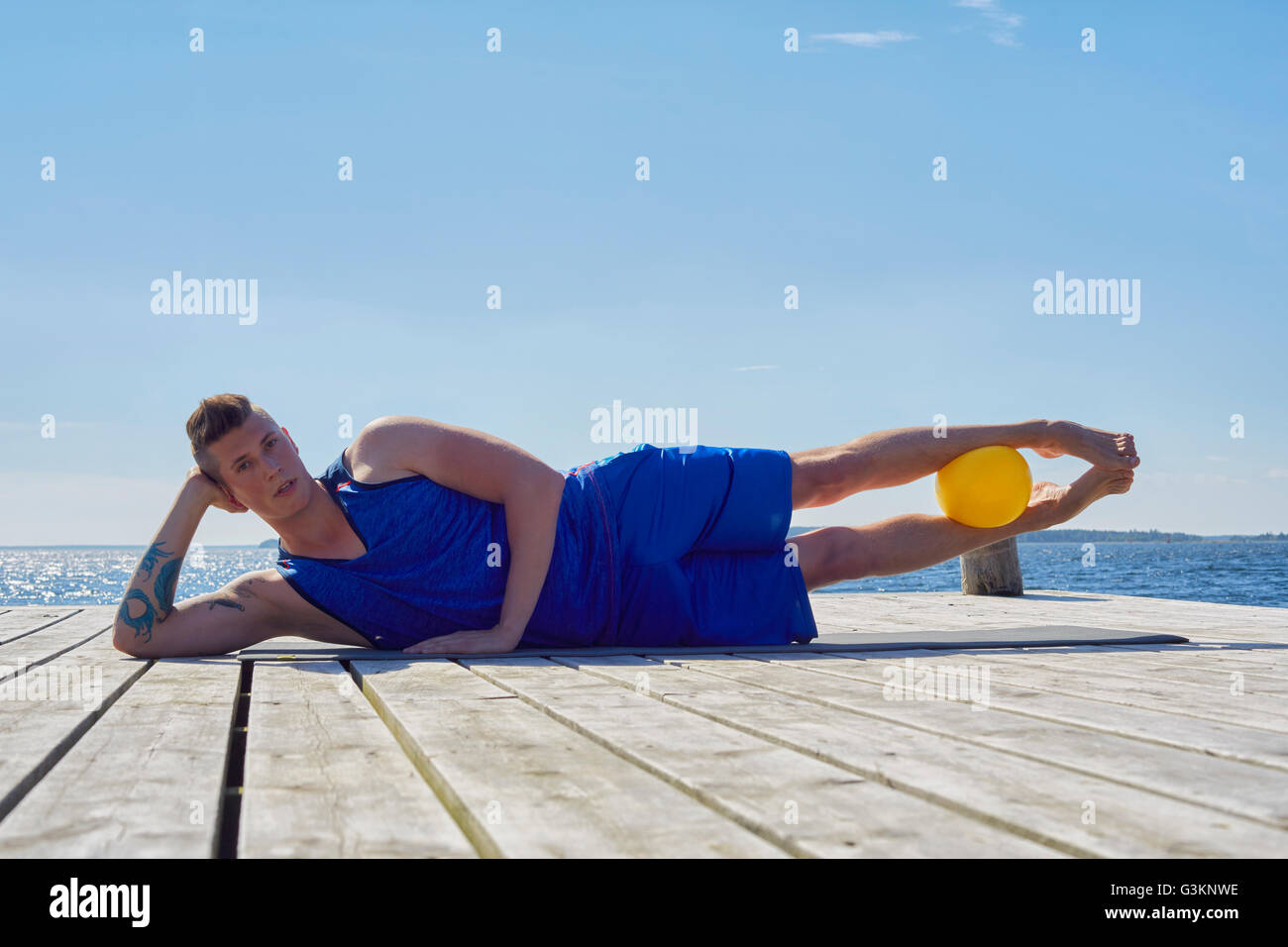 Man lying on side on pier, resting on elbow ball between legs looking at camera Stock Photo