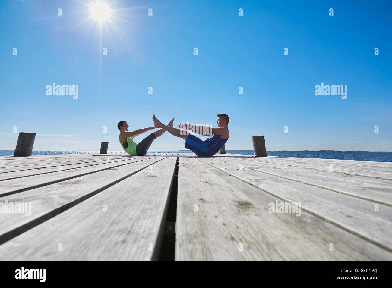 Mid distance view of couple on pier face to face doing sit ups Stock Photo