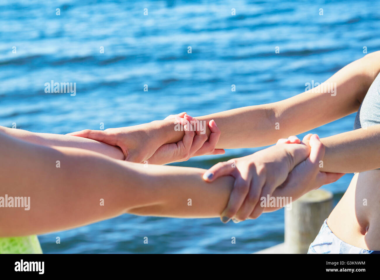 Cropped view of women in front of ocean holding into each others wrists Stock Photo