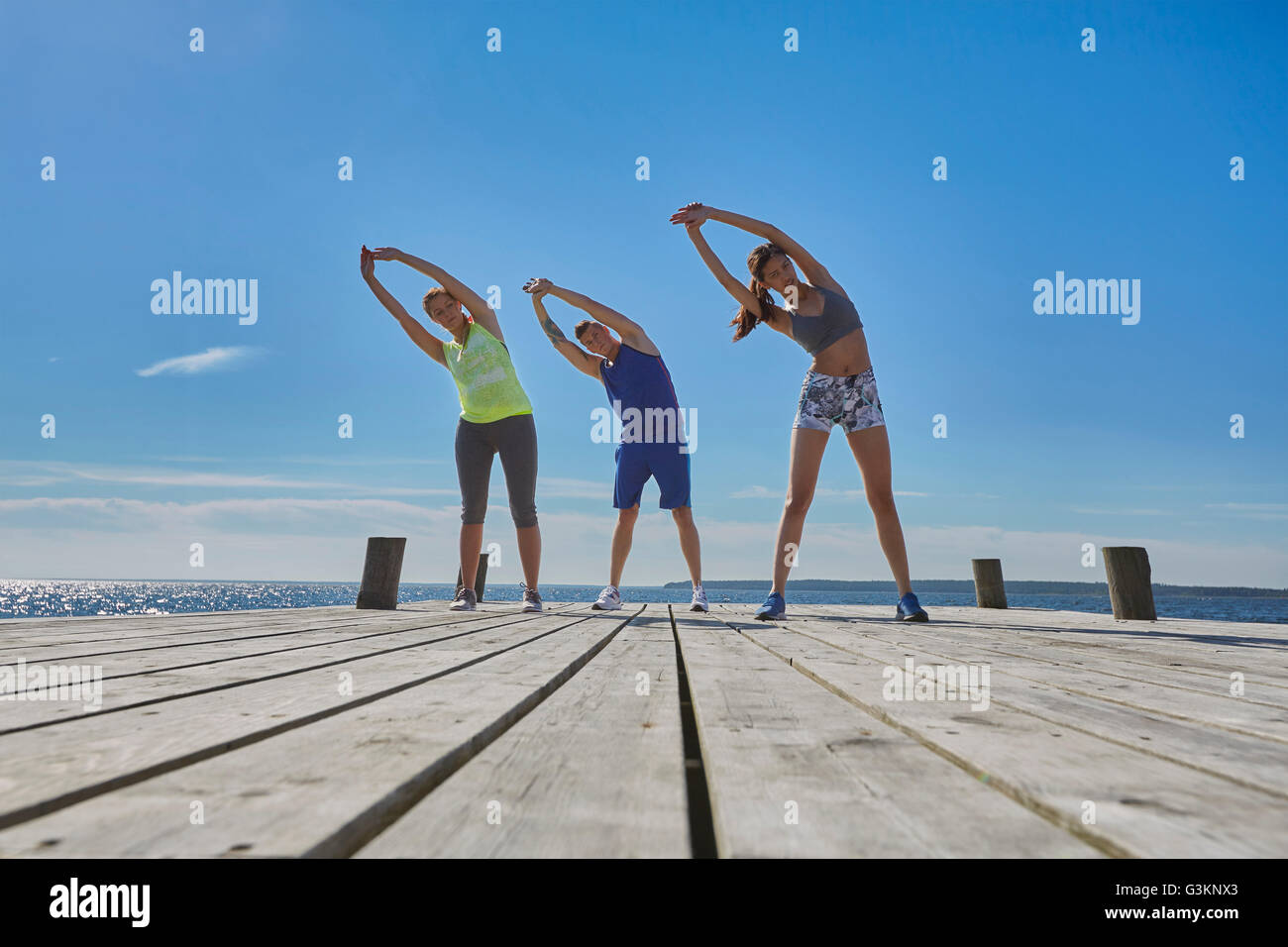 Friends on pier side by side arms raised bending over sideways stretching Stock Photo