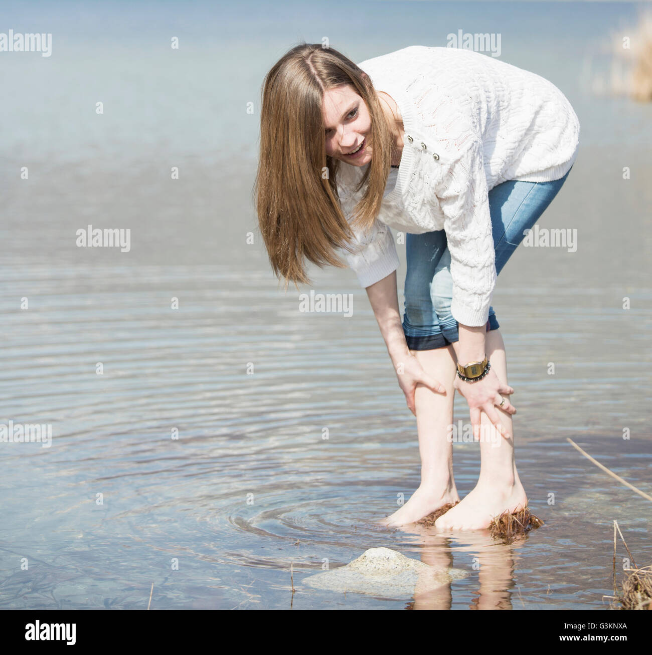 Teenage girl with jeans rolled up ankle deep in water bending forwards Stock Photo