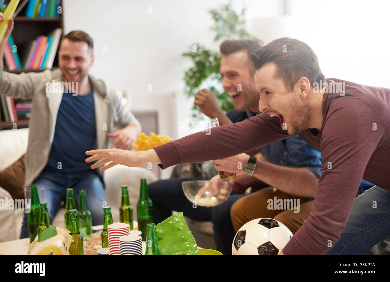 Group of men watching sporting event on television holding football celebrating Stock Photo