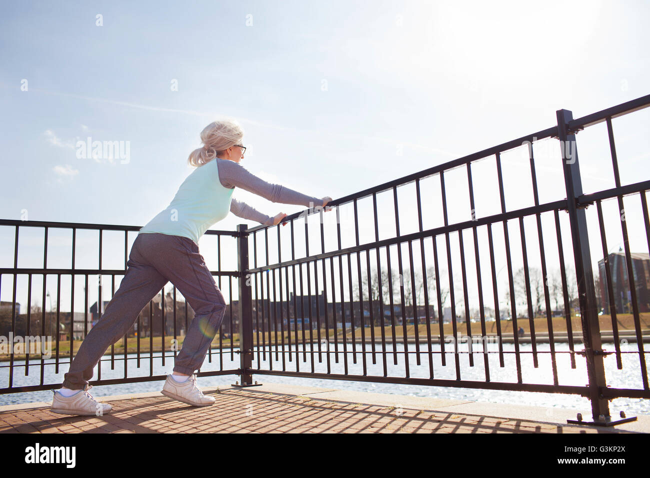 Full length side view of woman leaning against railing stretching Stock Photo