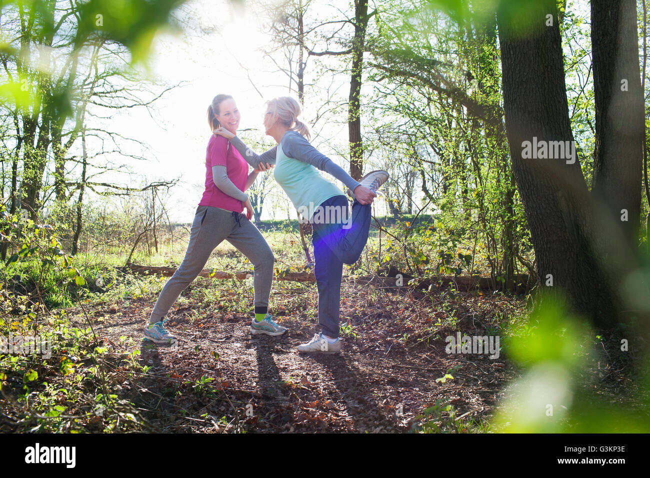 Side view of women in forest face to face holding ankle stretching leg Stock Photo