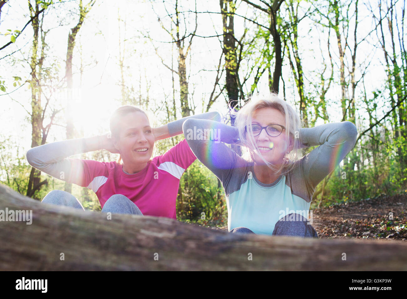 Women in forest hands behind head doing sit up against fallen tree Stock Photo