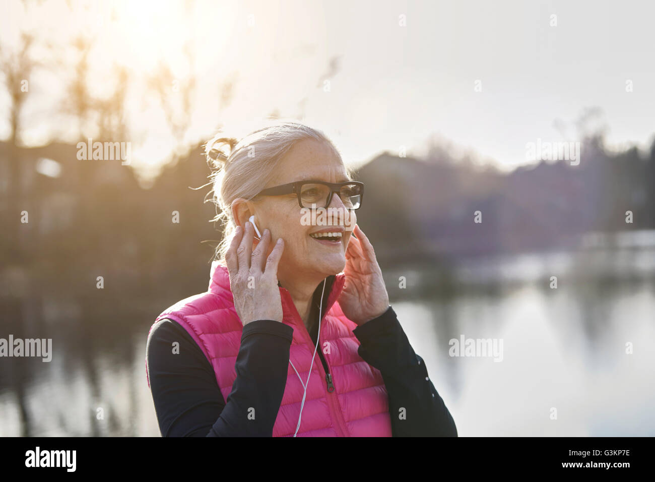 Woman wearing glasses and earbuds, hands on ears looking away smiling Stock Photo
