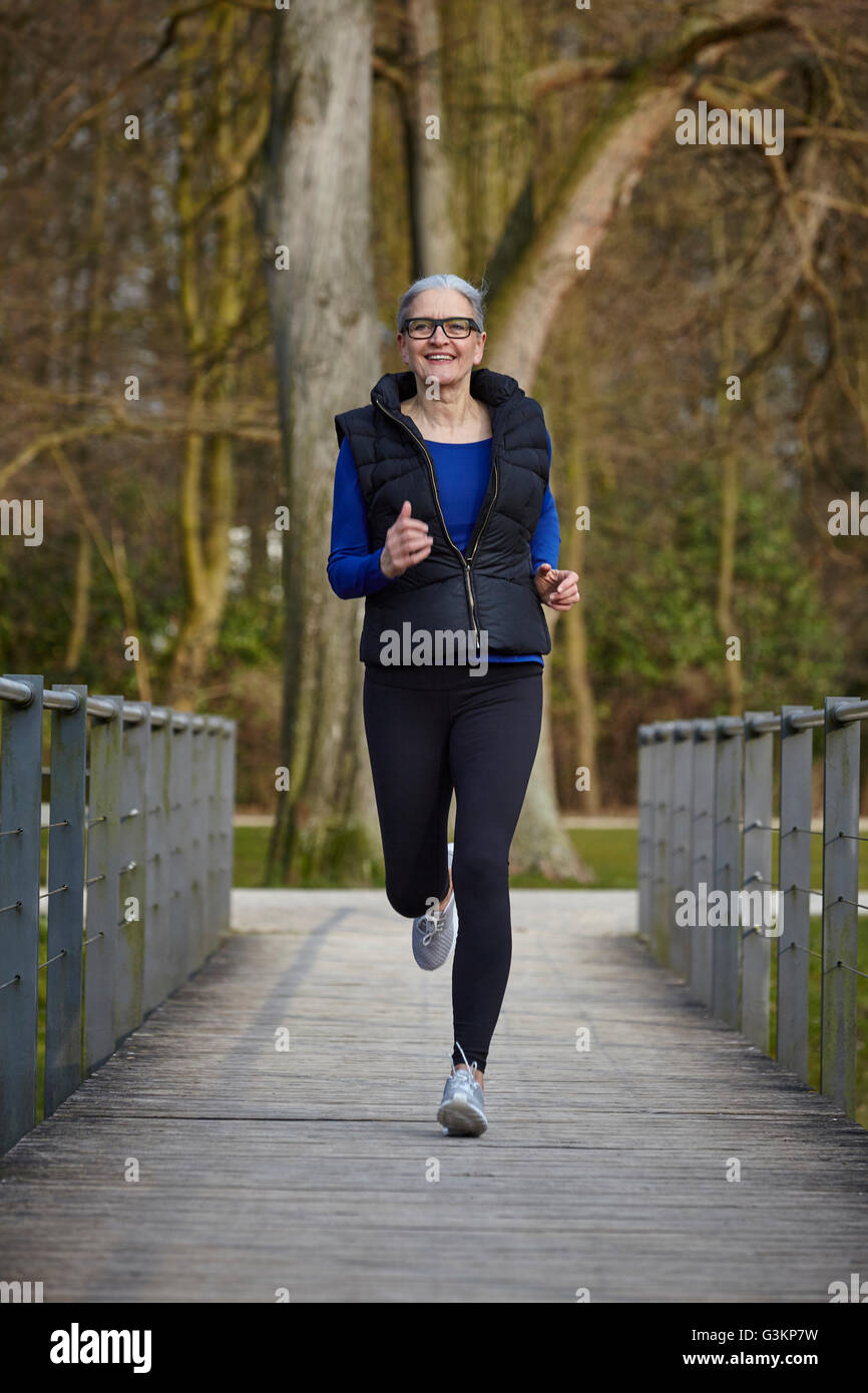 Full length front view of woman on wooden path jogging, looking at camera smiling Stock Photo