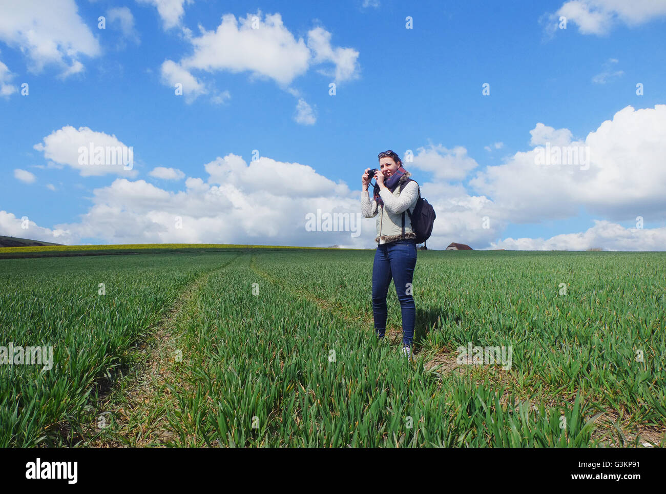 Young woman standing in field, taking photograph of landscape Stock Photo