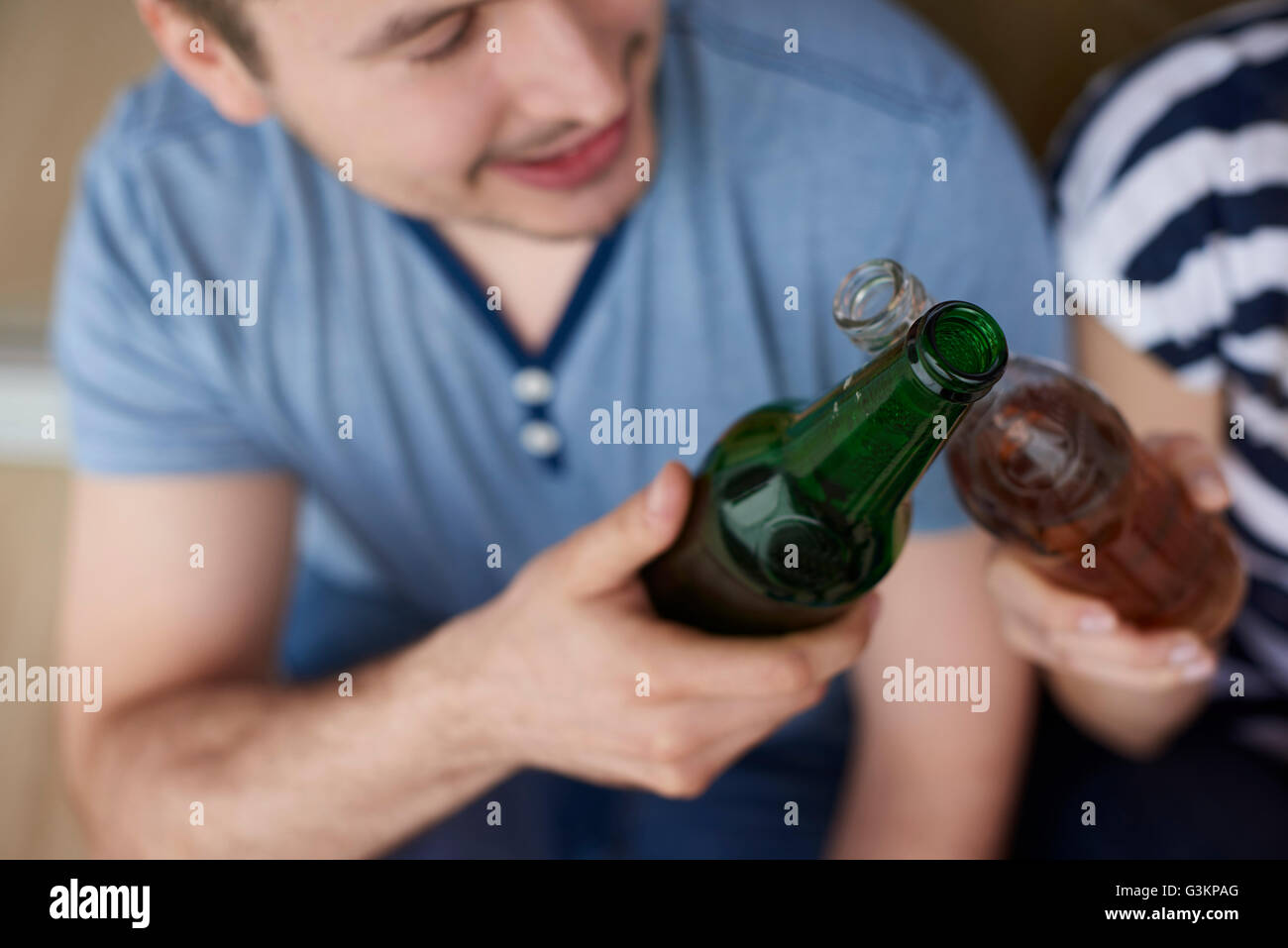 Young couple sitting outdoors, toasting with bottled beers Stock Photo