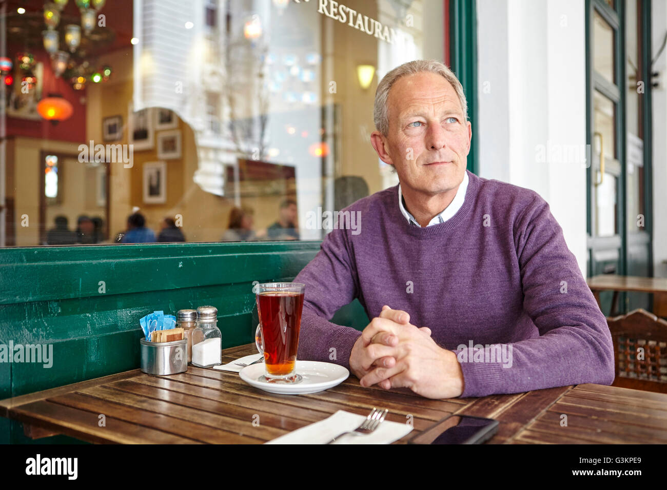 Mature man looking out from sidewalk cafe table Stock Photo