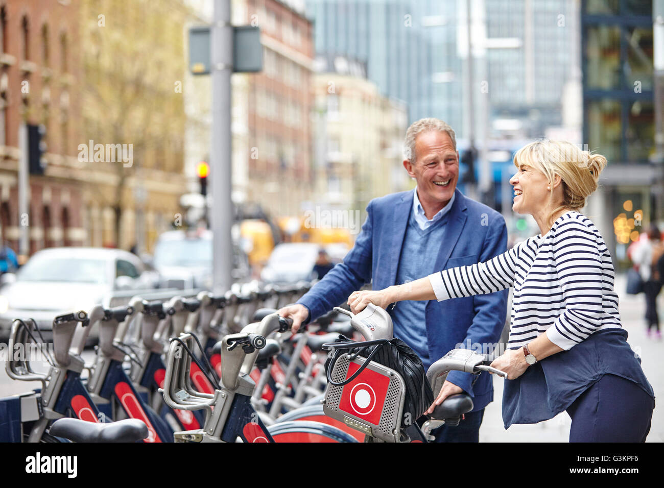 Mature dating couple removing hire bicycles from rack, London, UK Stock Photo