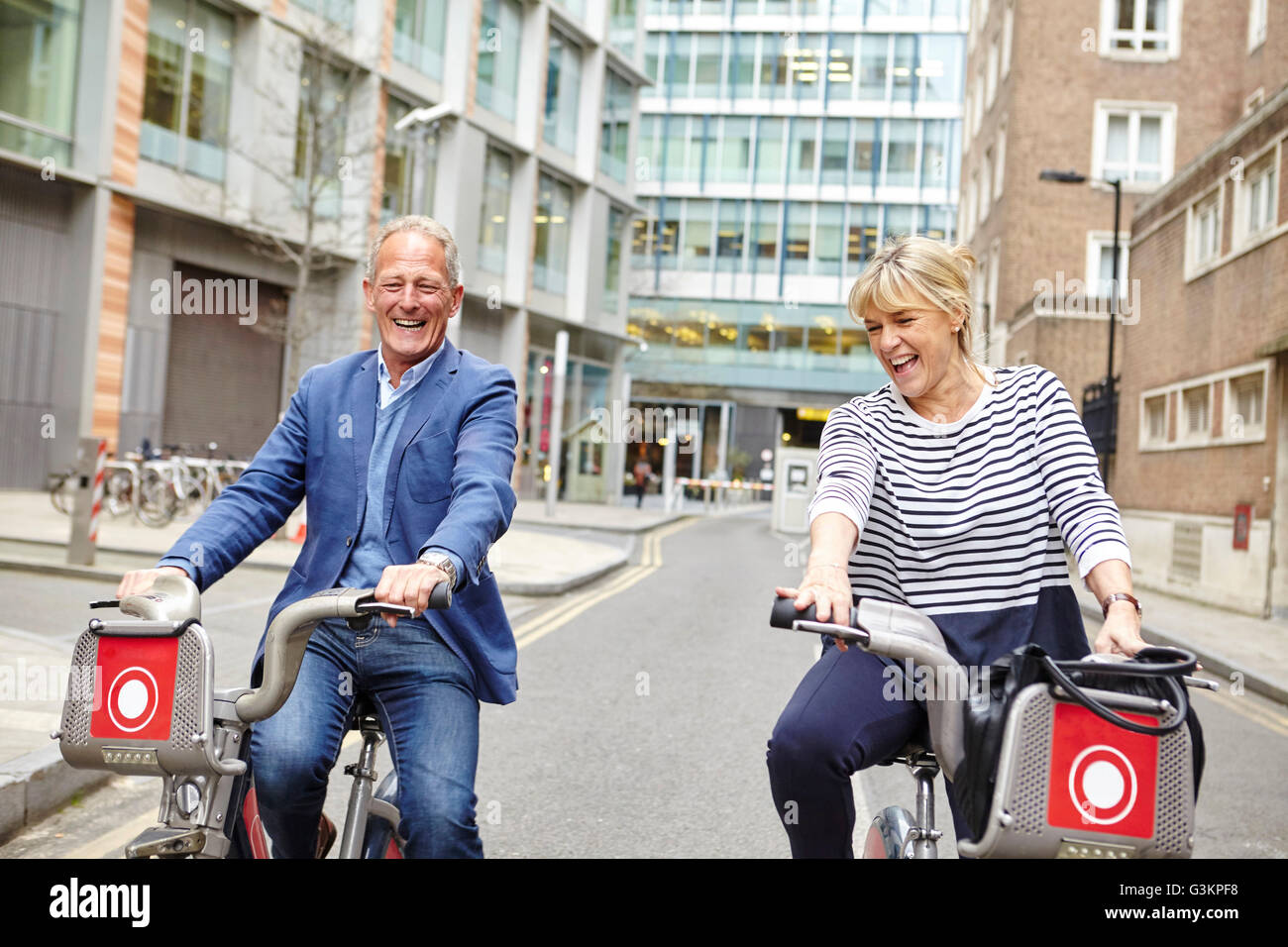 Mature dating couple laughing whilst cycling on hire bicycles, London, UK Stock Photo