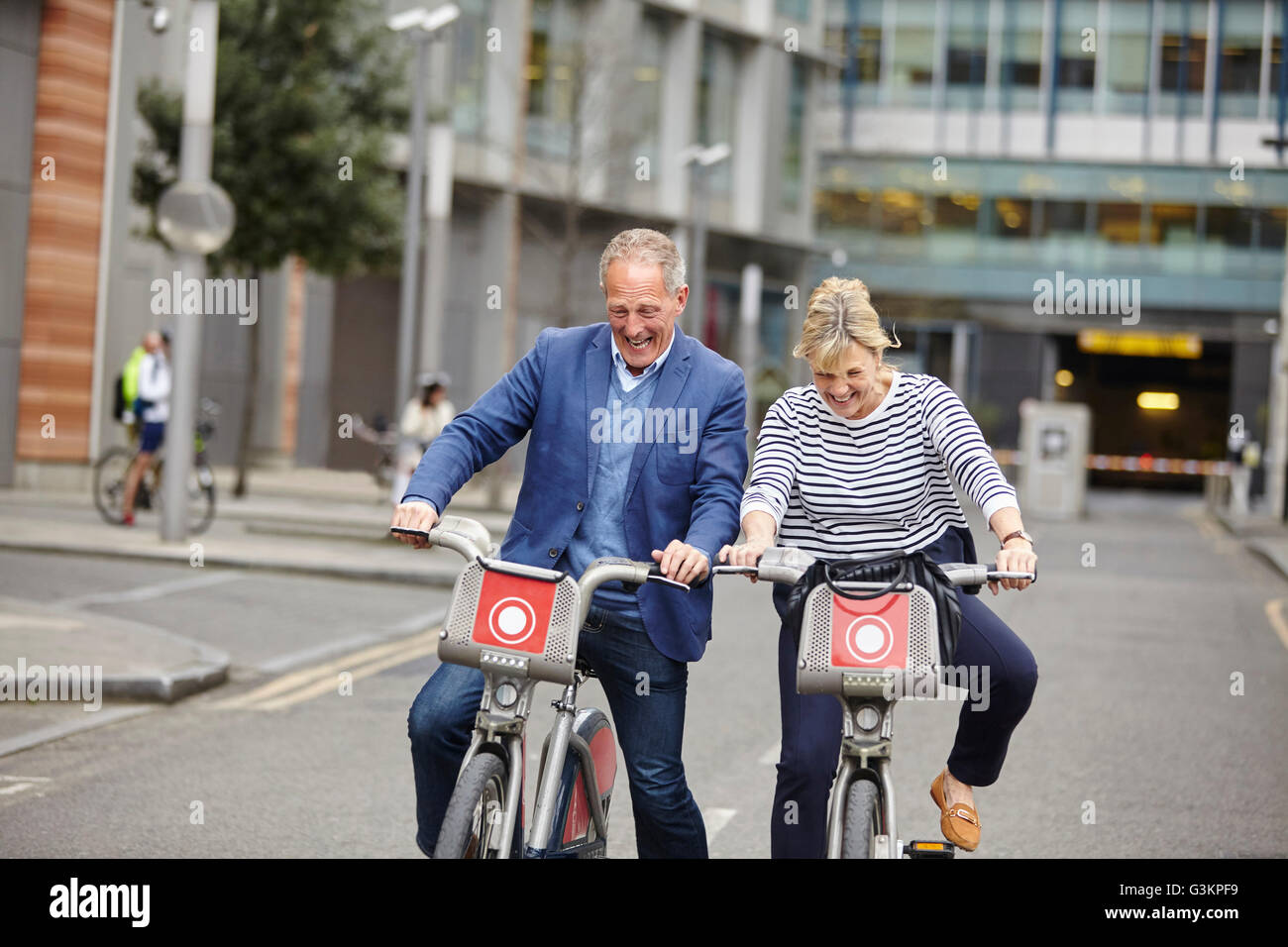 Mature dating couple laughing whilst cycling on hire bicycles, London, UK Stock Photo