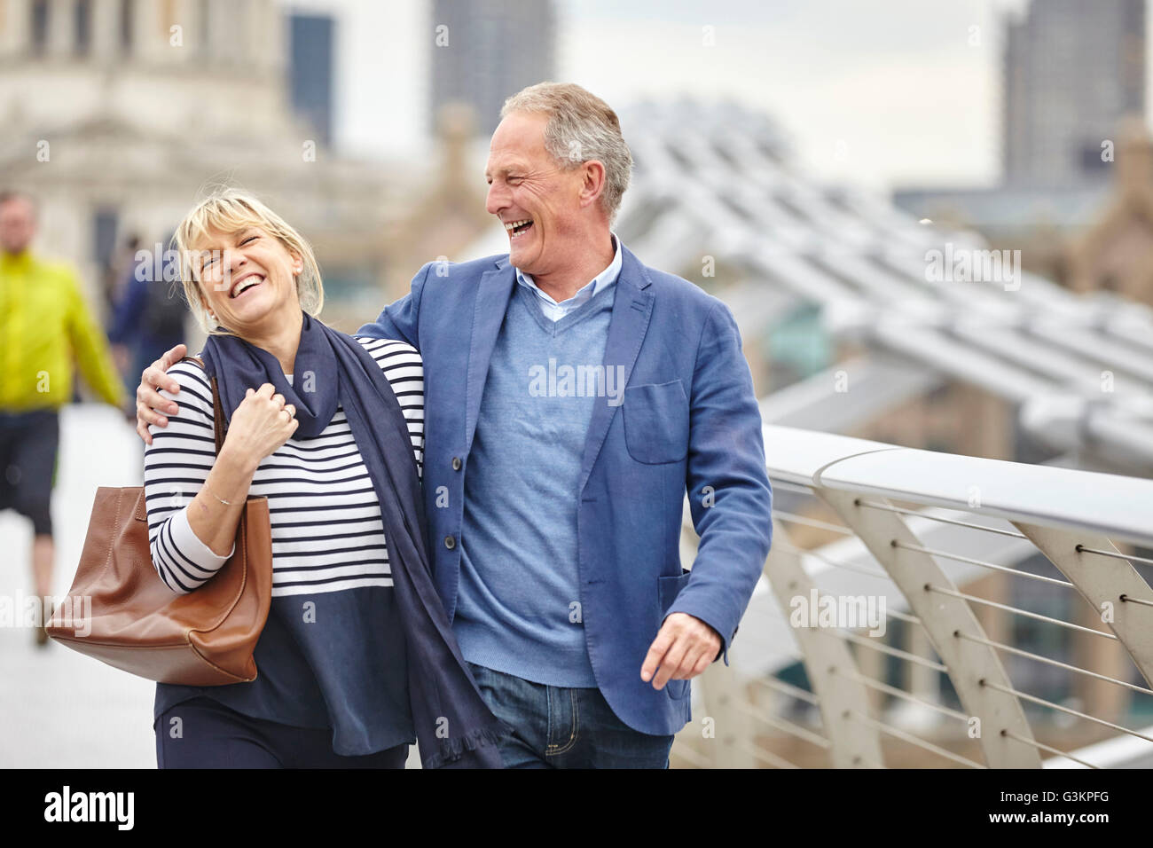 Mature dating couple laughing whilst crossing Millennium Bridge, London, UK Stock Photo
