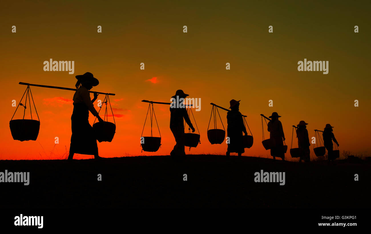 Silhouette of workers carrying yoke and buckets at sunset, Myanmar