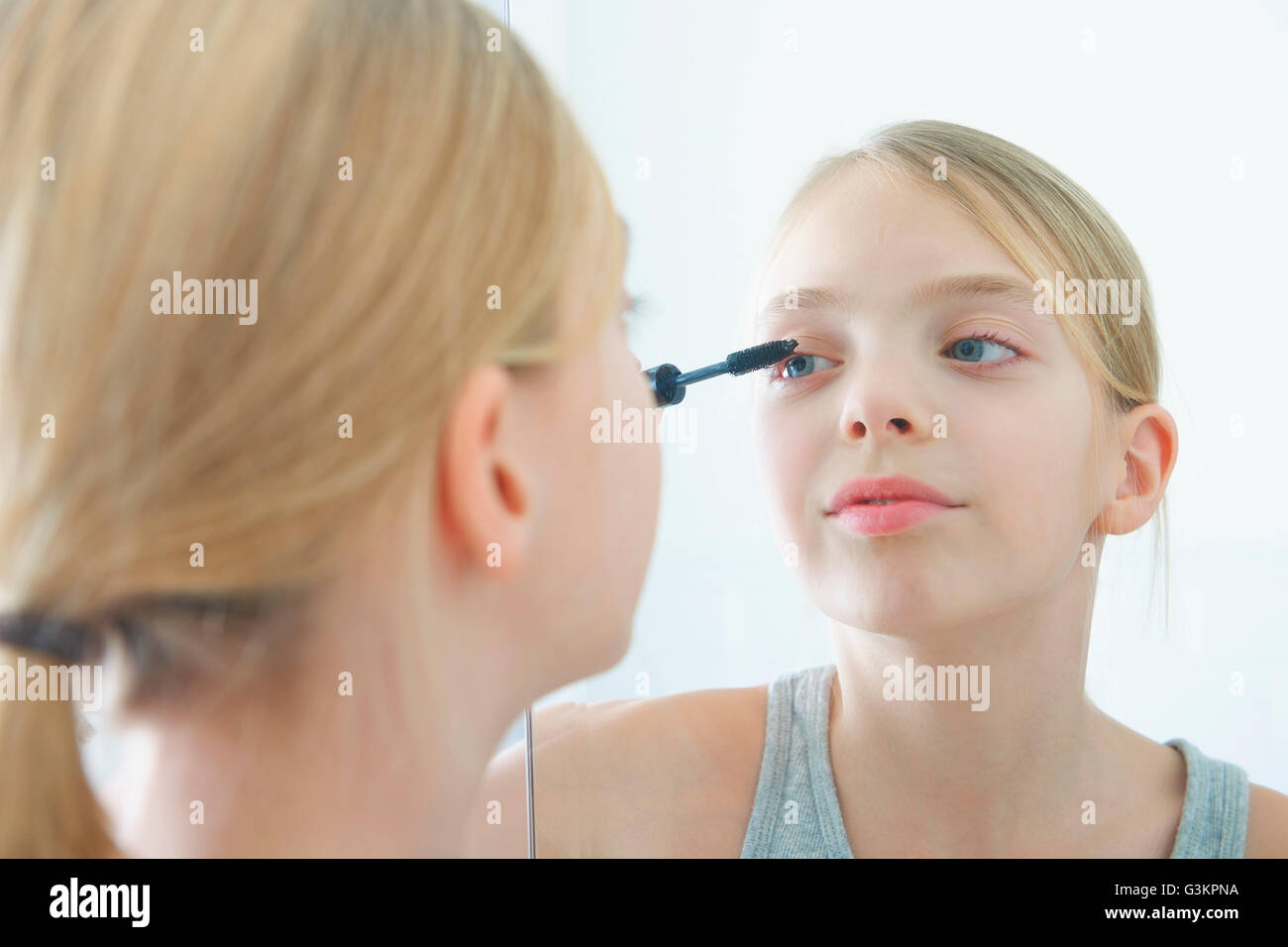 Over the shoulder mirror image of girl applying mascara Stock Photo
